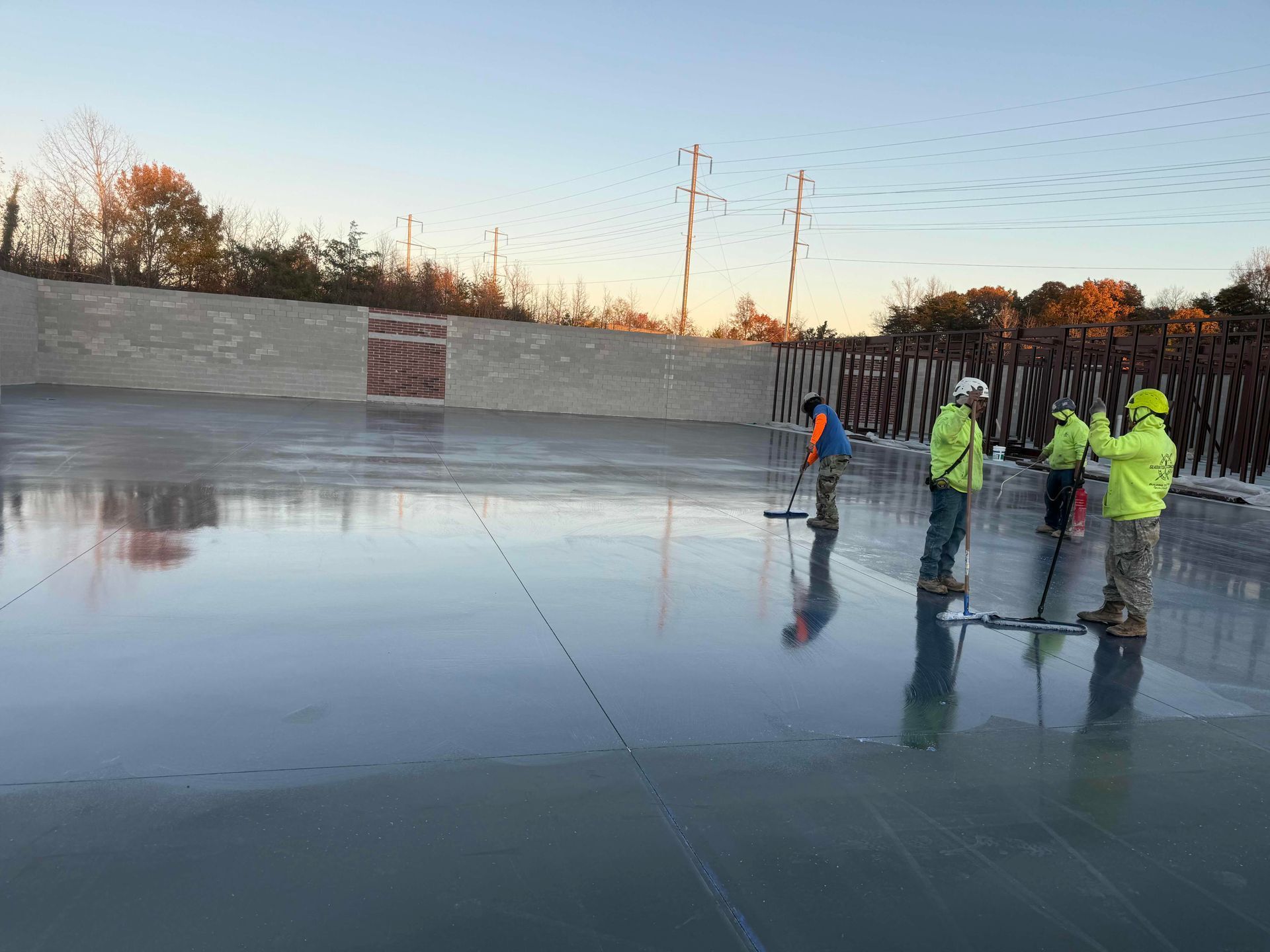 Workers on an icy outdoor court, spraying water to resurface it at sunset.