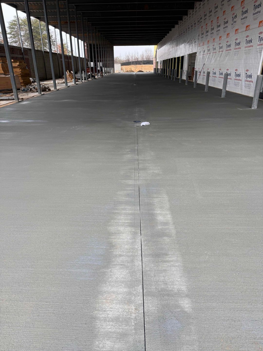 Empty indoor construction area with a smooth gray concrete floor and exposed framing along the sides.