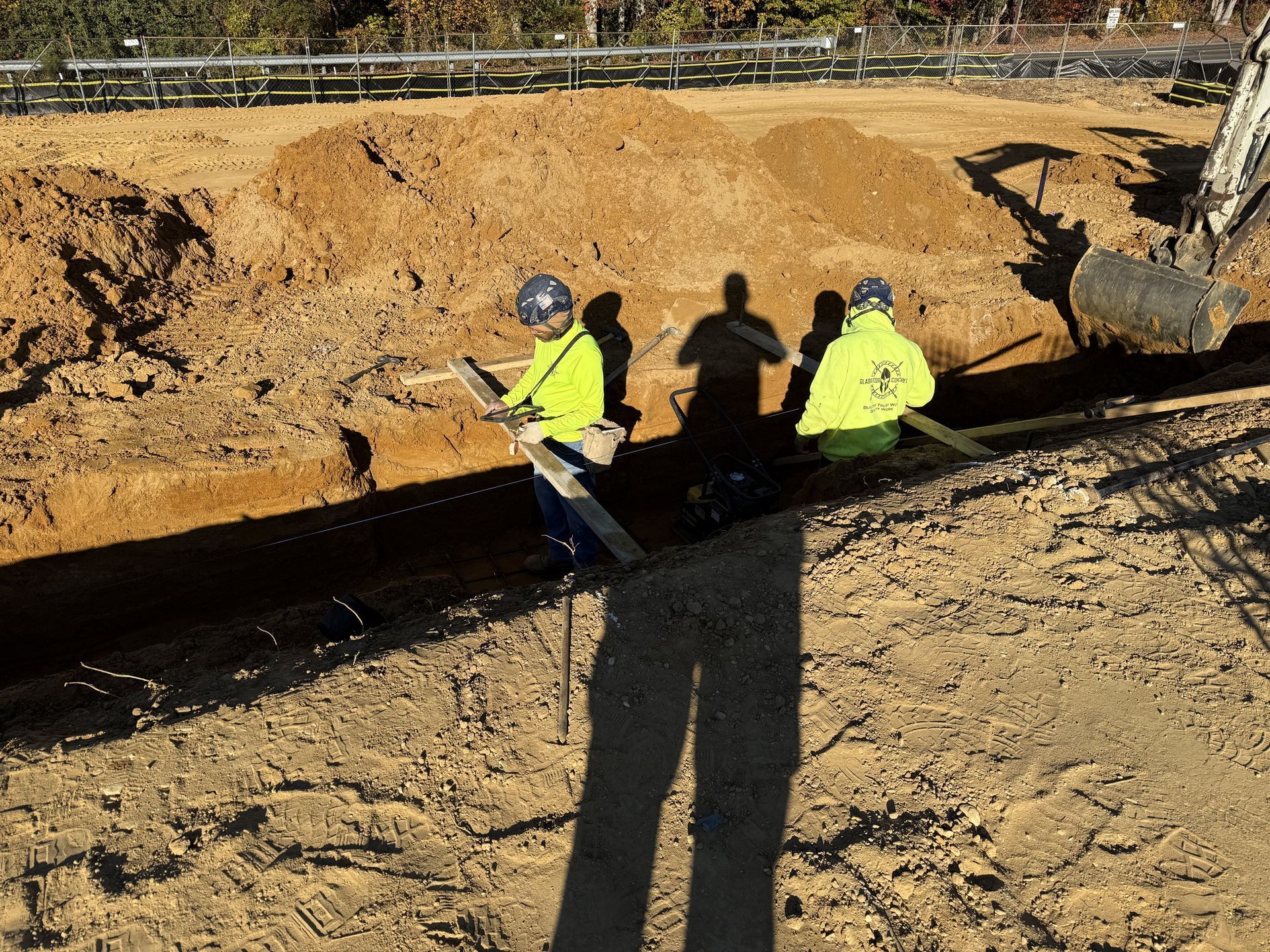 Workers in yellow safety jackets inspecting a trench at a dirt construction site