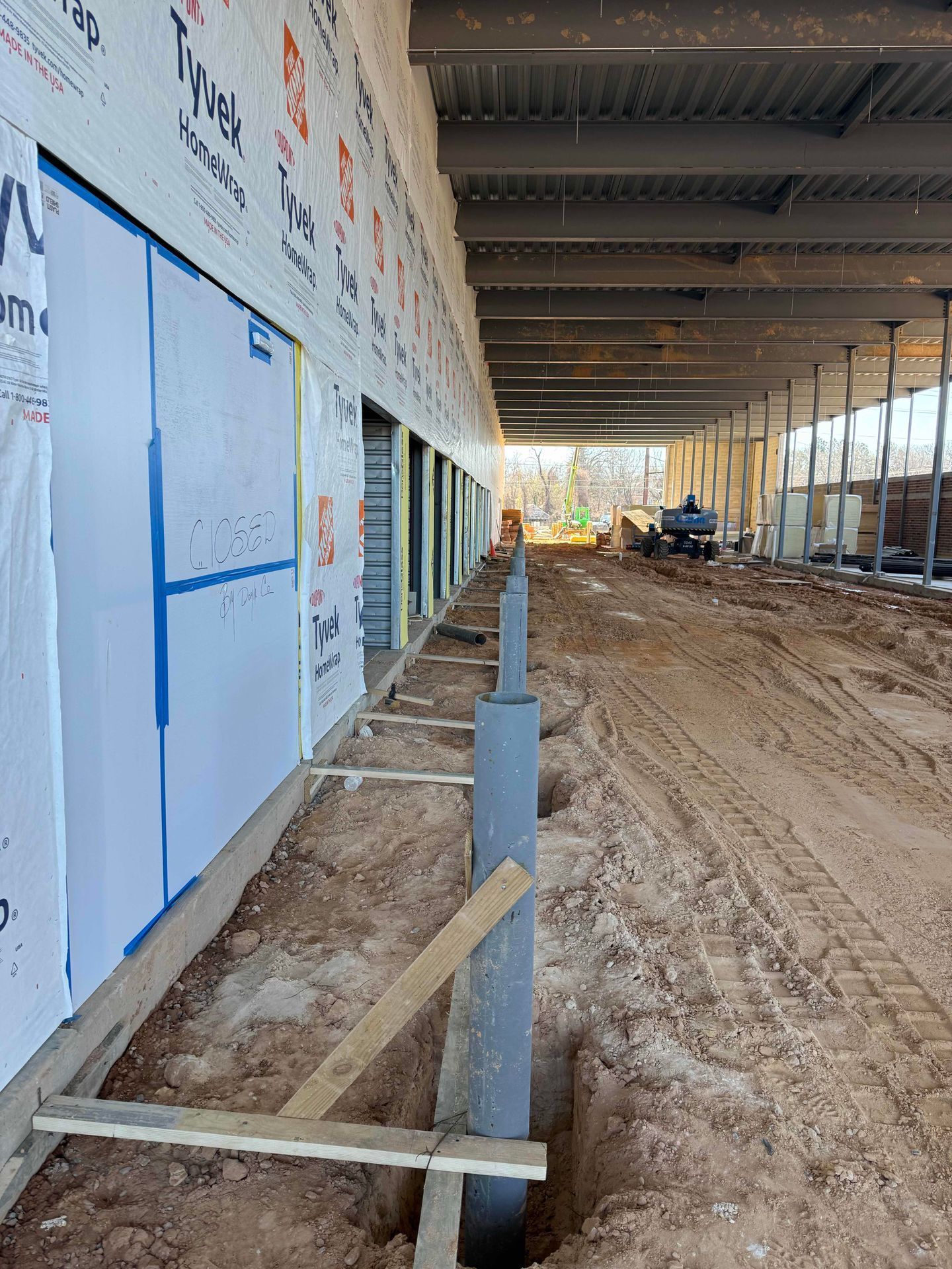 Construction site corridor with dirt floor, metal posts, and blue wall panels under a roofed structure