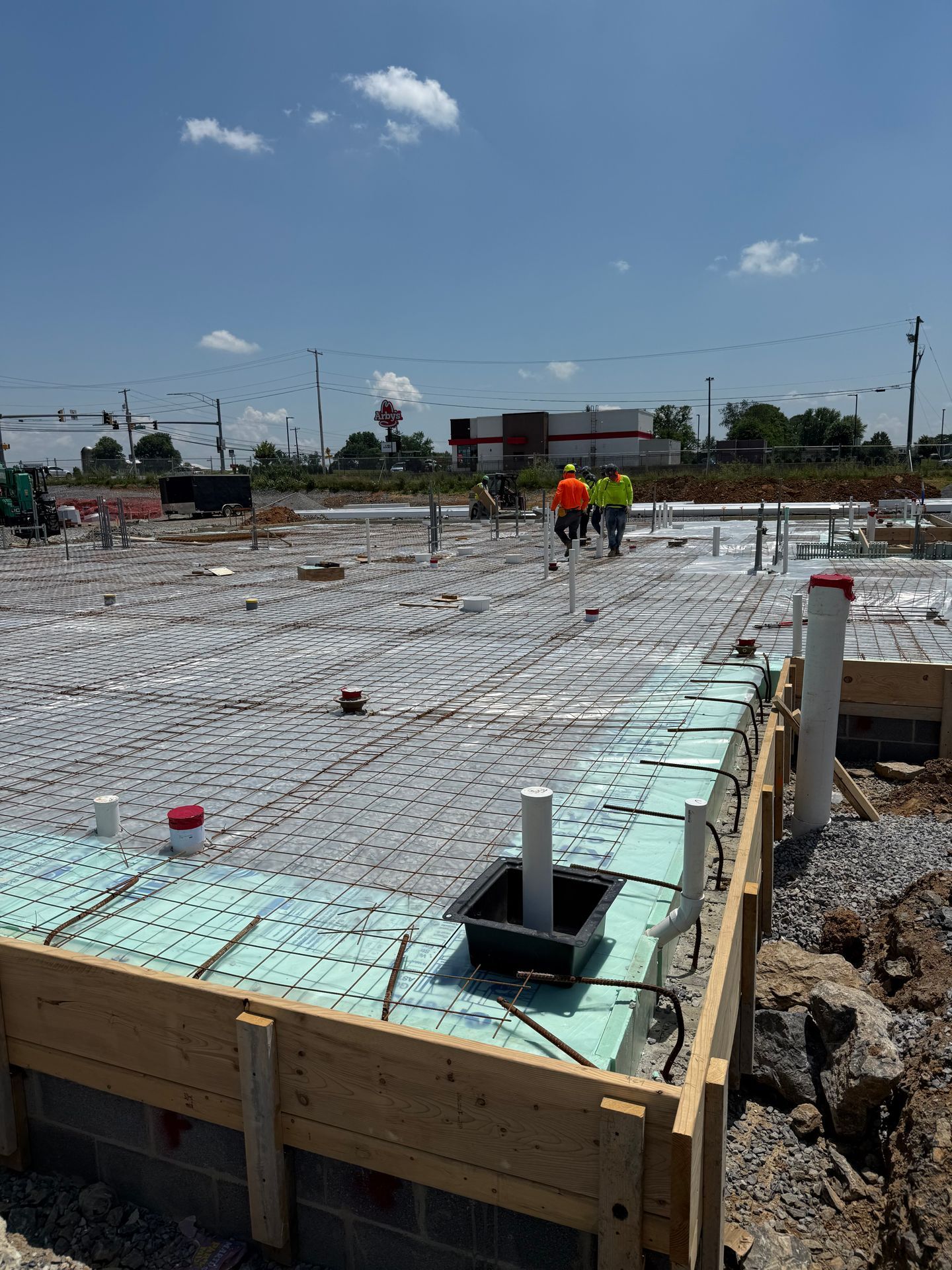 Construction site with rebar and concrete forms, two workers in orange vests under a clear sky