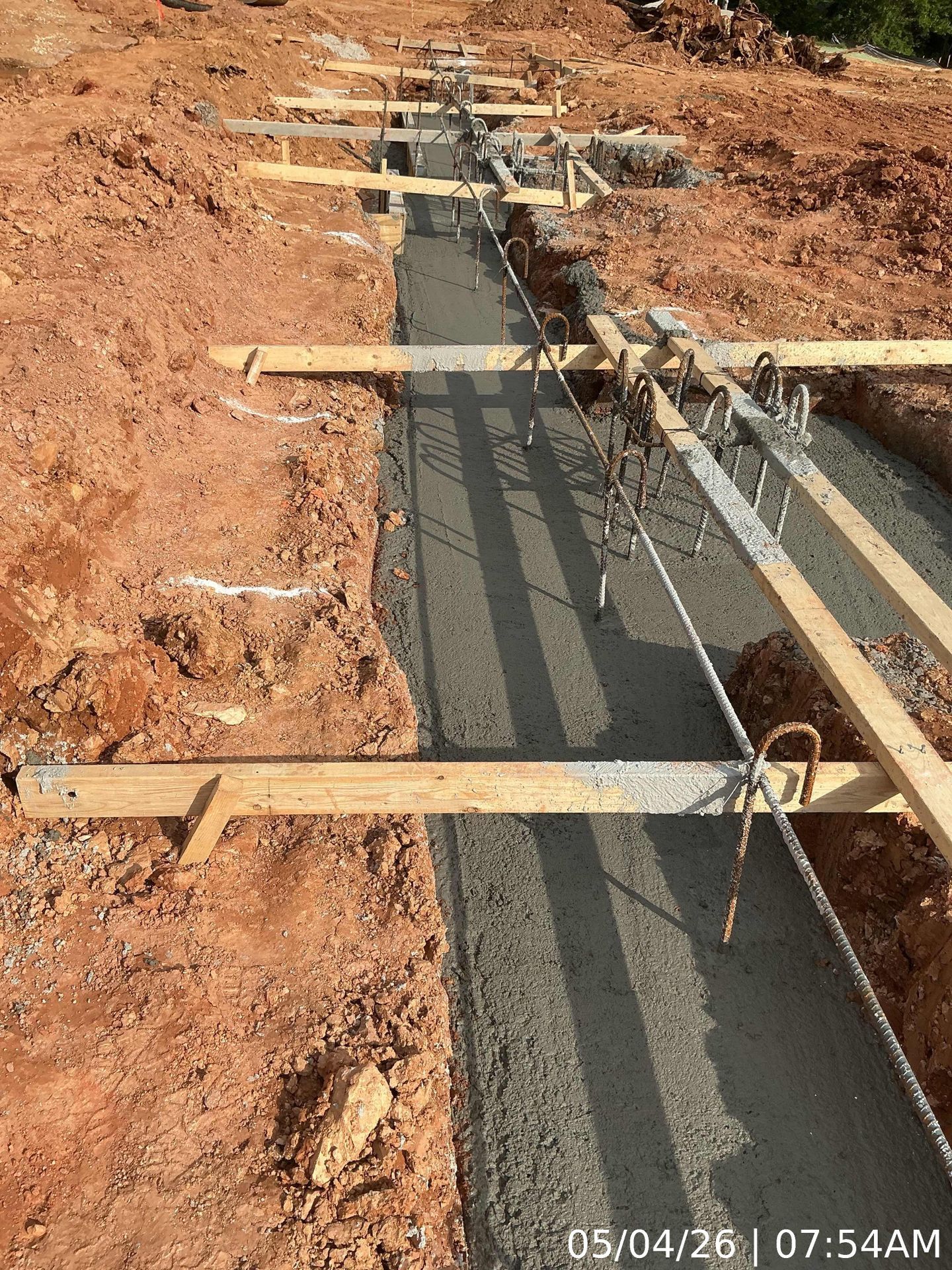 Concrete trench under construction with wooden forms and steel rebar in red dirt