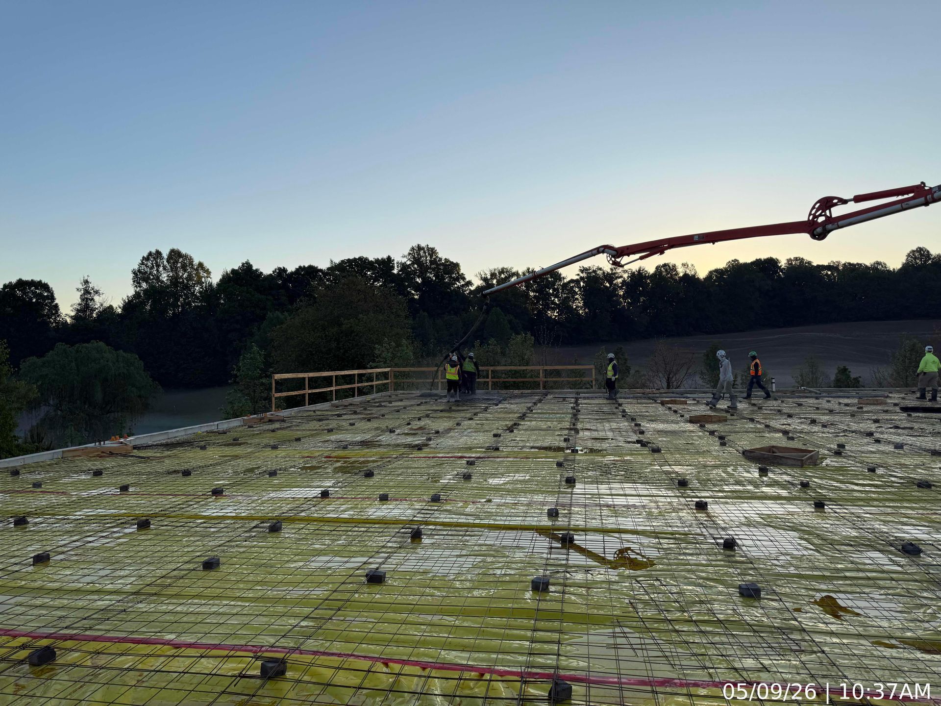 Construction workers pouring a concrete slab at dawn, with rebar grid and pump boom visible.