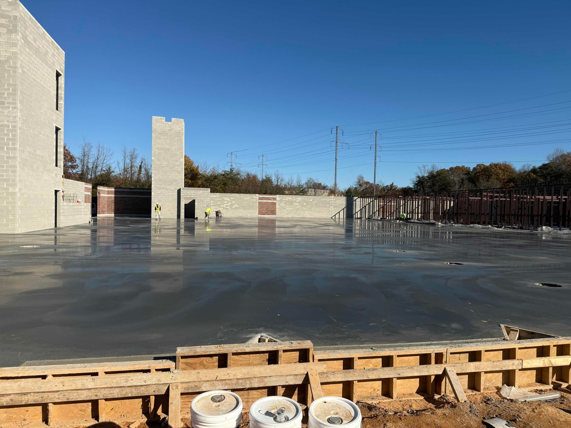 Empty concrete courtyard with a stone wall, blue sky, and construction materials in the foreground