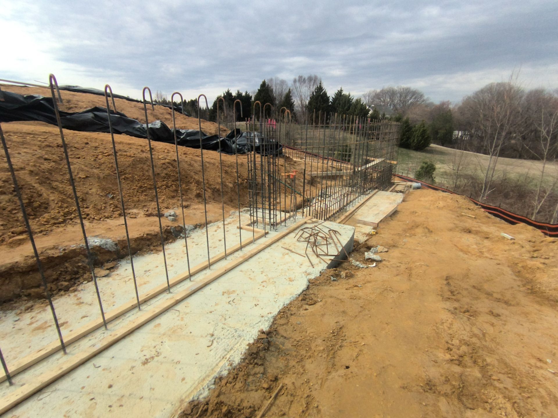 Foundation rebar and concrete footings along a dirt construction site on a hillside