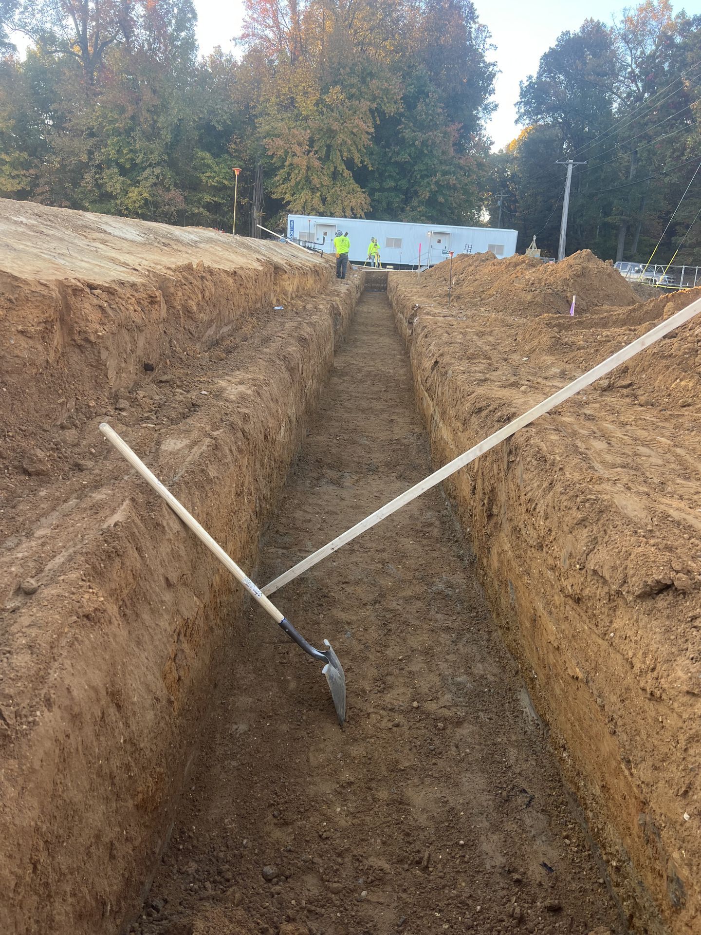 Trenched excavation site with a shovel in the center and caution tape marking the area outdoors