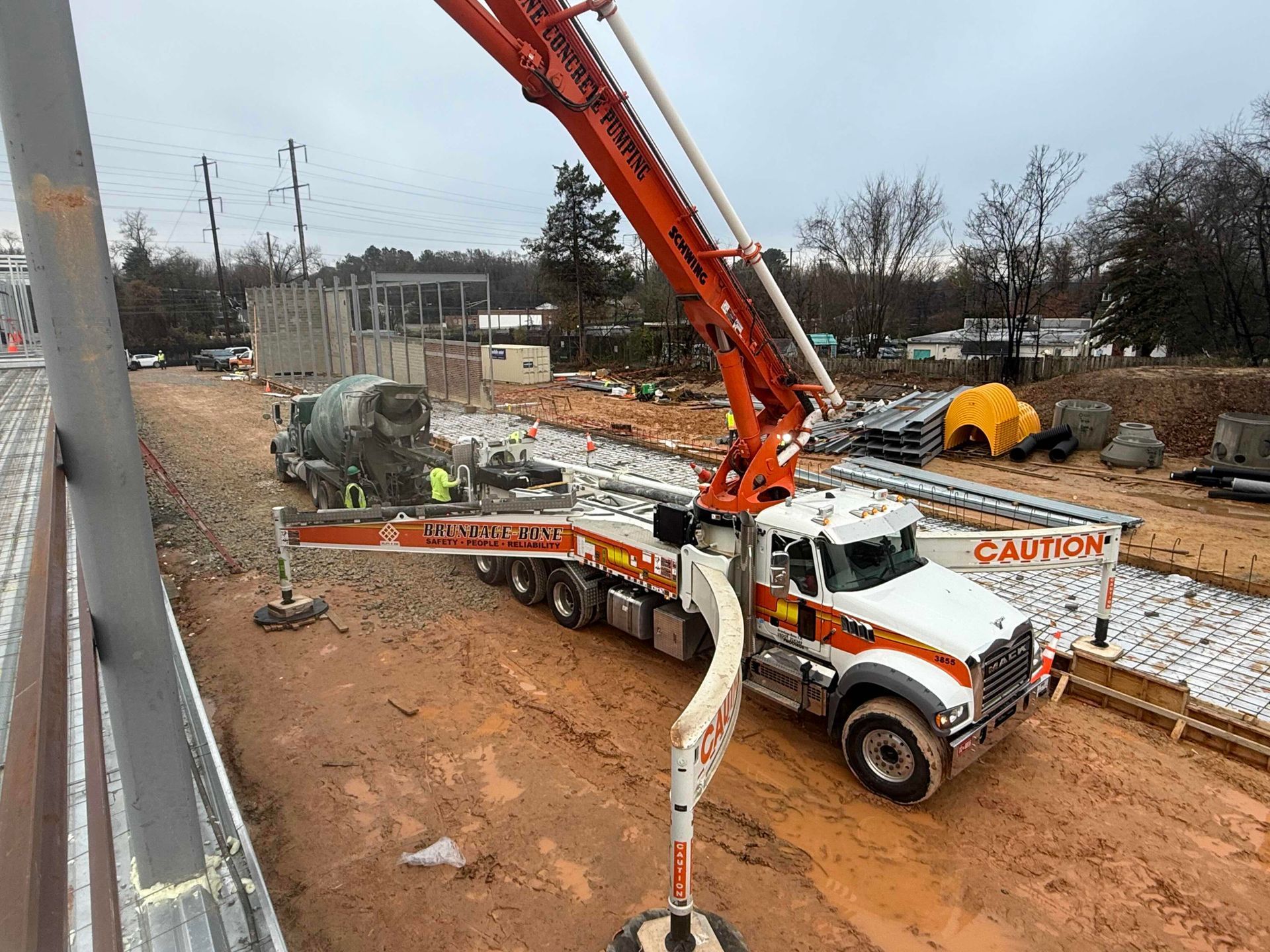 Orange concrete pump truck pouring concrete at a roadside construction site
