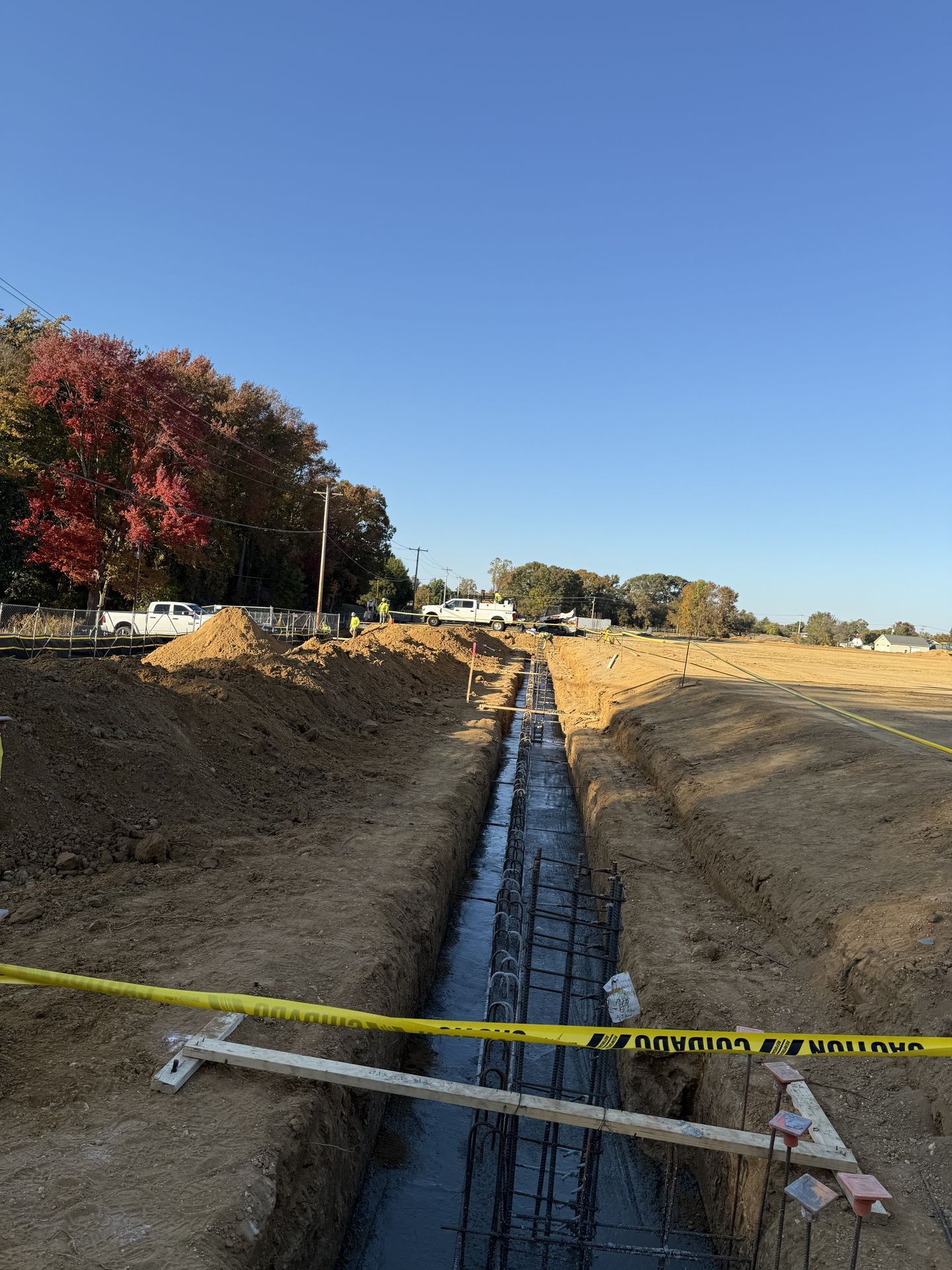 Trench excavation with concrete drainage channel under construction, marked by caution tape along a dirt site.