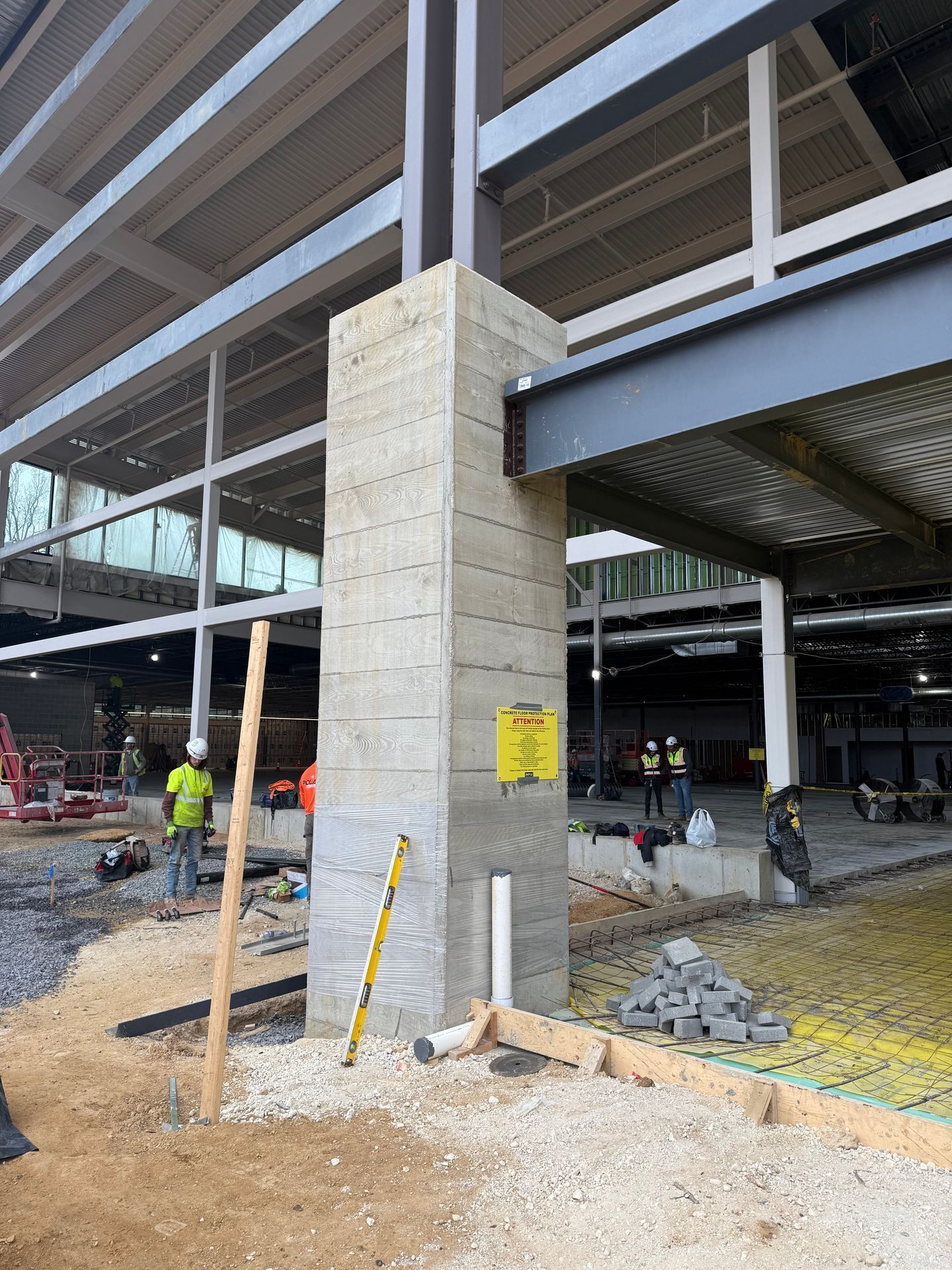 Construction site with concrete column beneath a steel-framed building and workers in the background