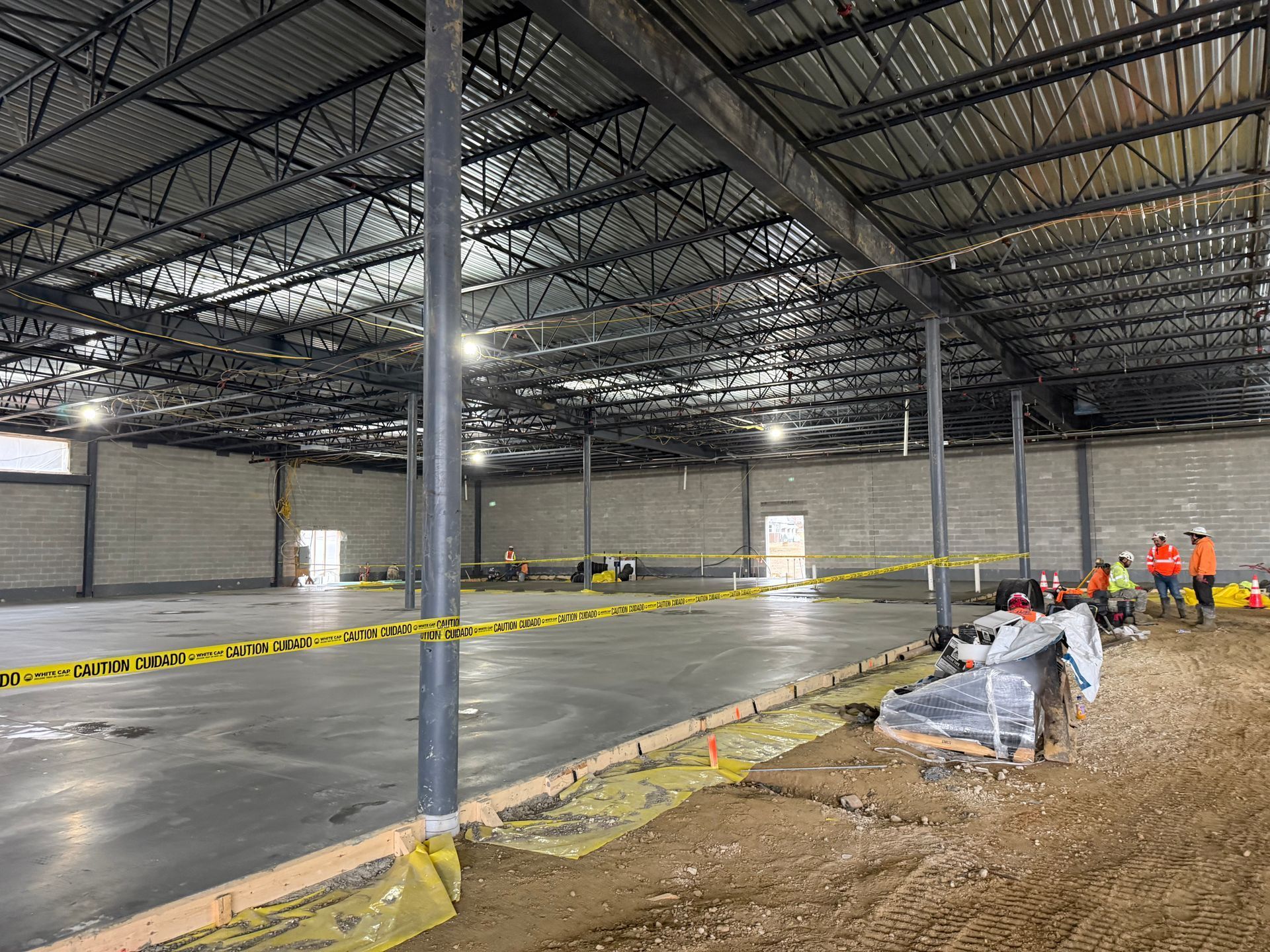 Large warehouse interior under construction, with concrete floor, steel columns, caution tape