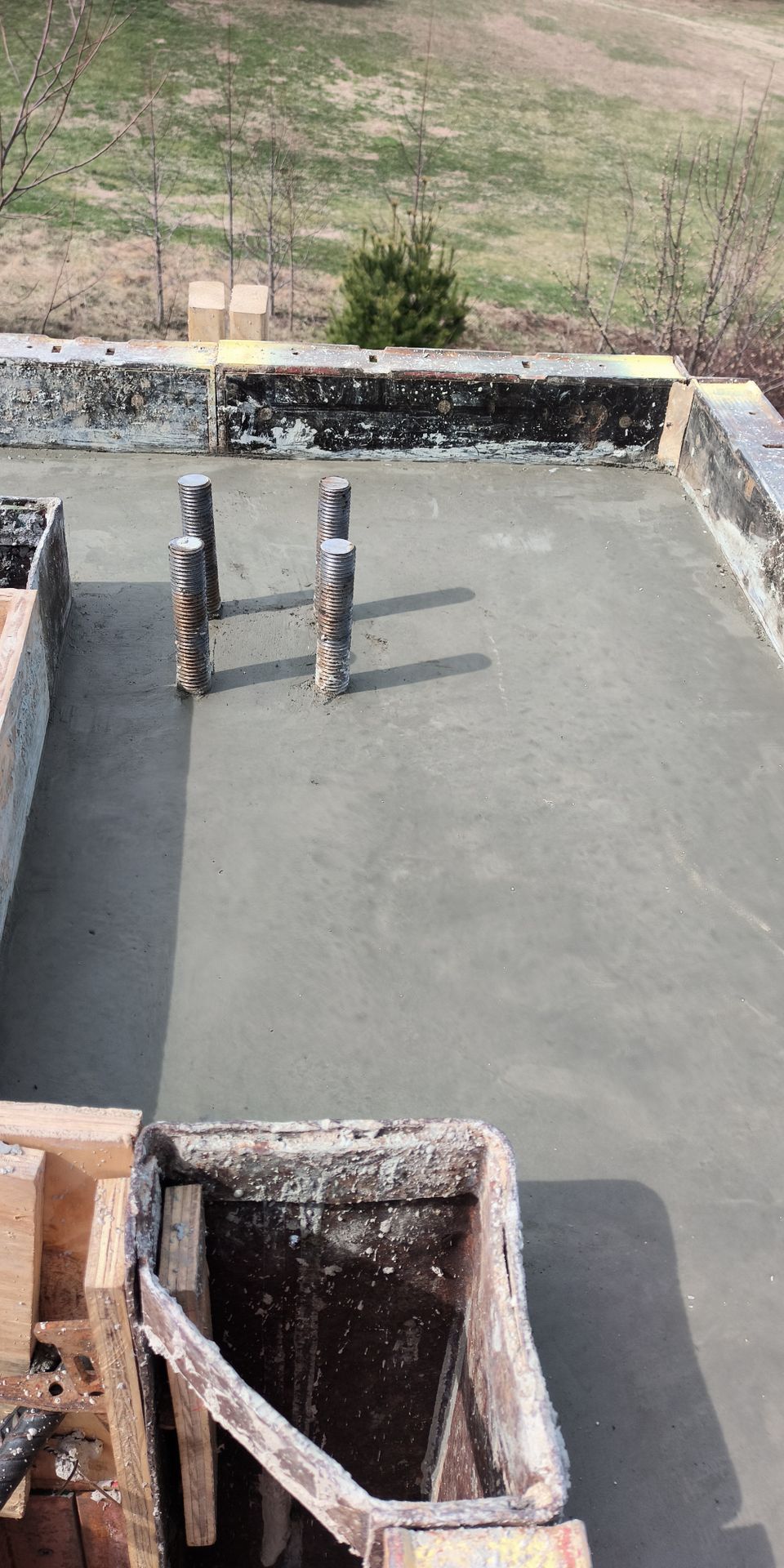 Rooftop under construction with concrete floor, short wall, and two vertical pipes or posts.