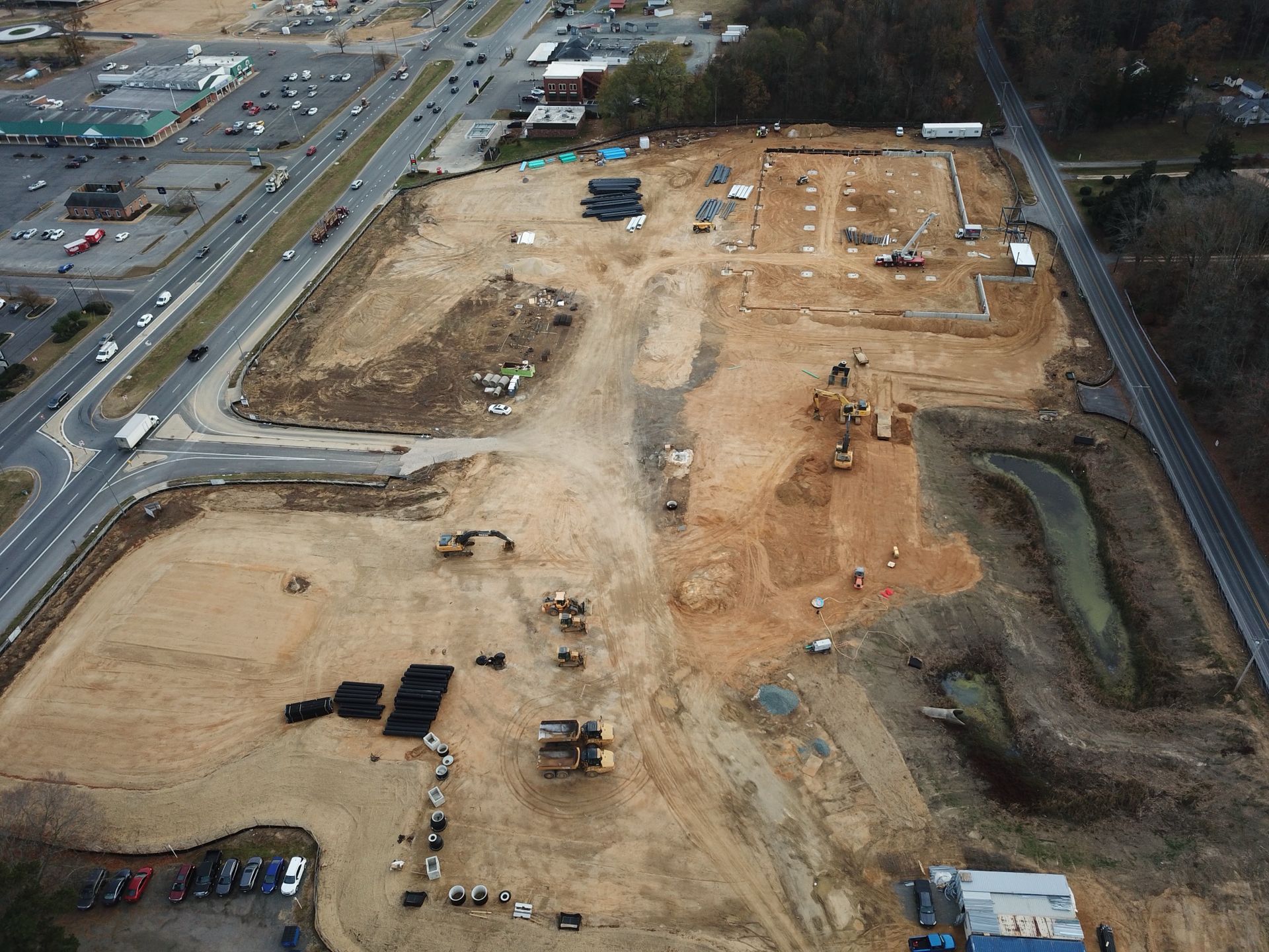 Aerial view of a large construction site beside a road, with dirt lots and excavation equipment.