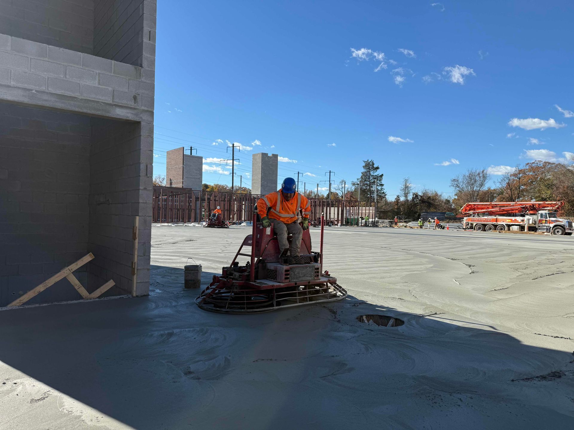 Worker using a power trowel smoothing wet concrete beside a building on a construction site