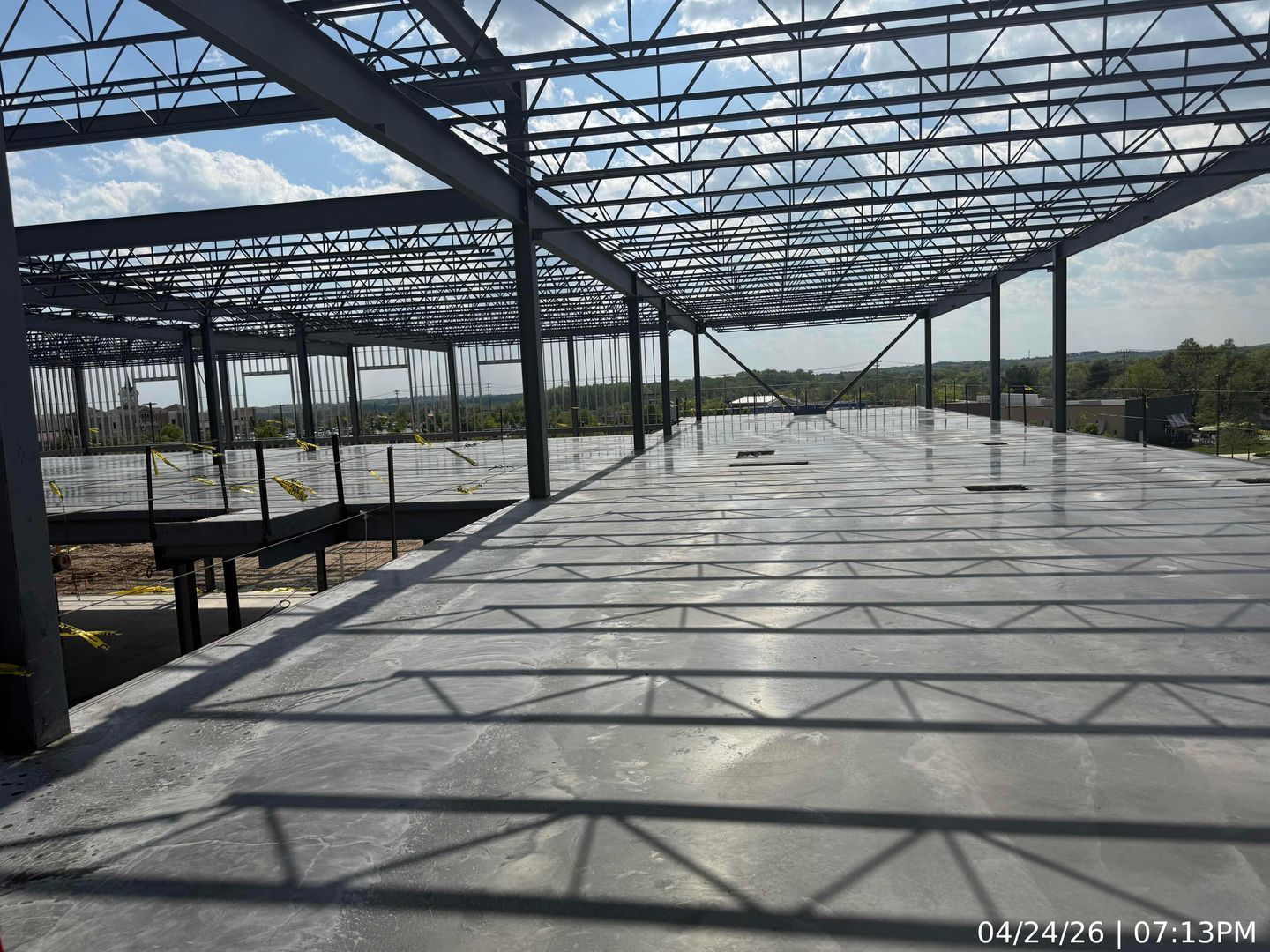 Empty steel-frame greenhouse under construction with glass roof and concrete floor under blue sky