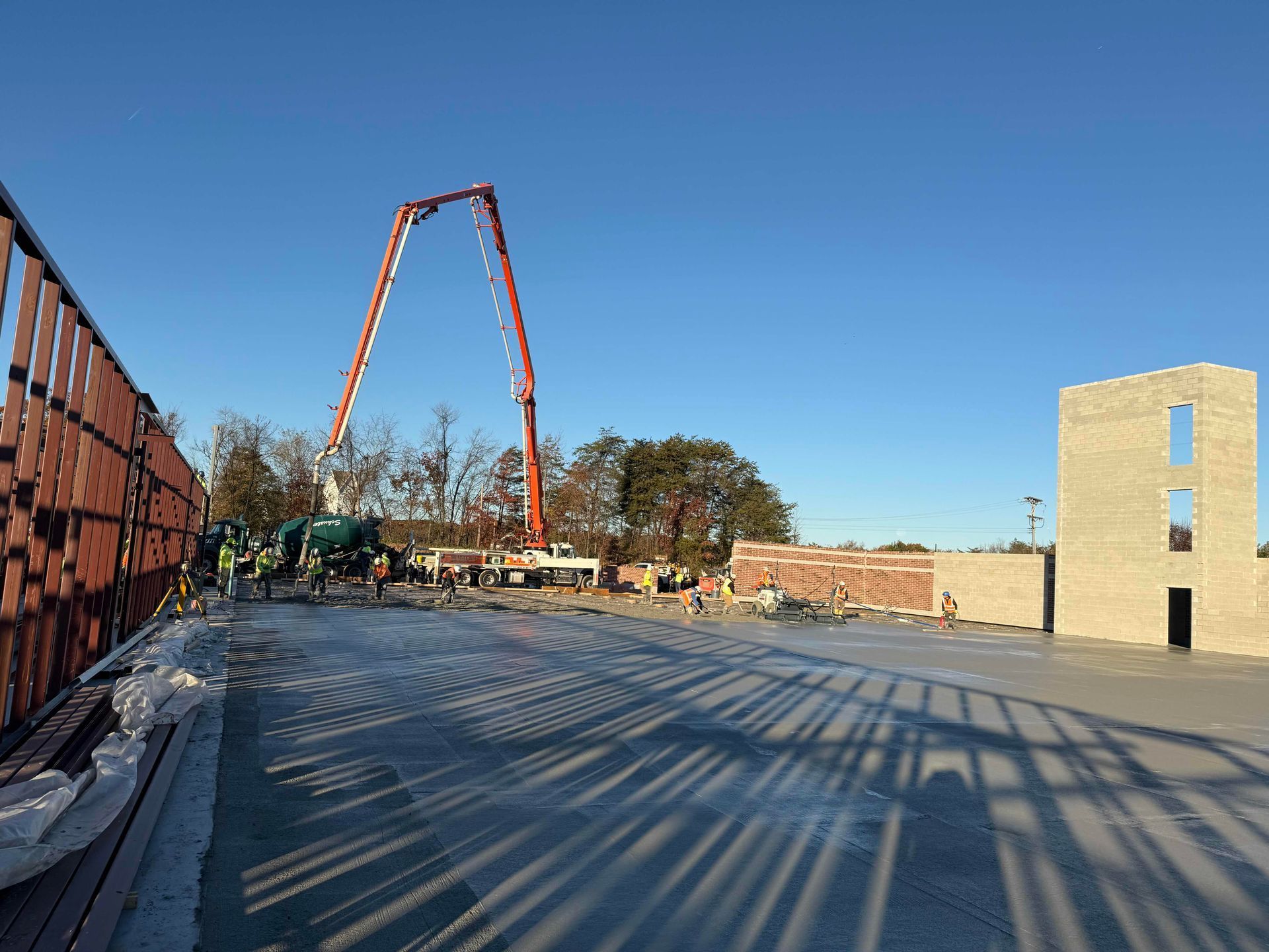 Construction site with concrete slab, orange boom pump, and workers under a clear blue sky