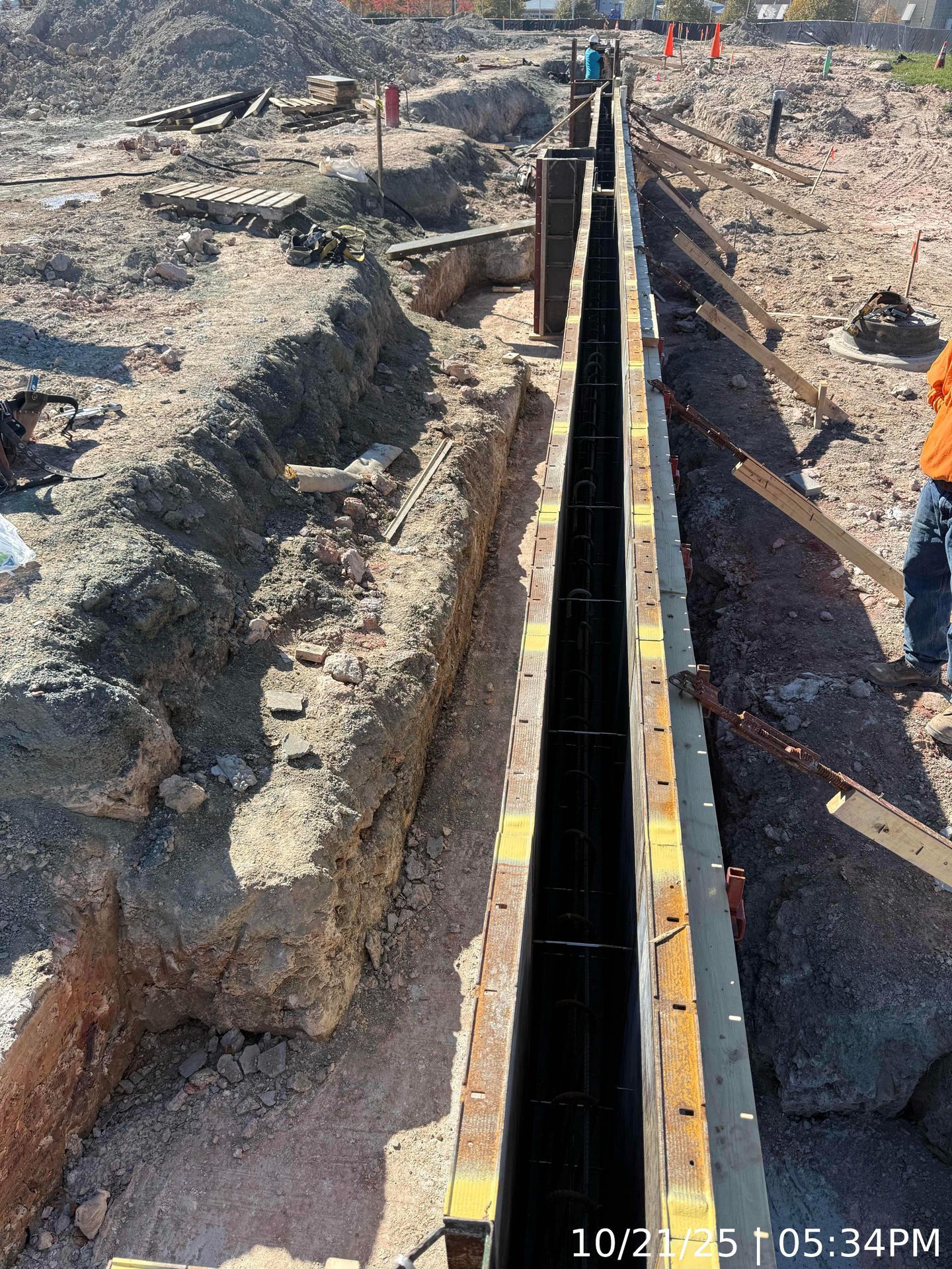 Long trench with a black pipeline being installed in a dusty construction site