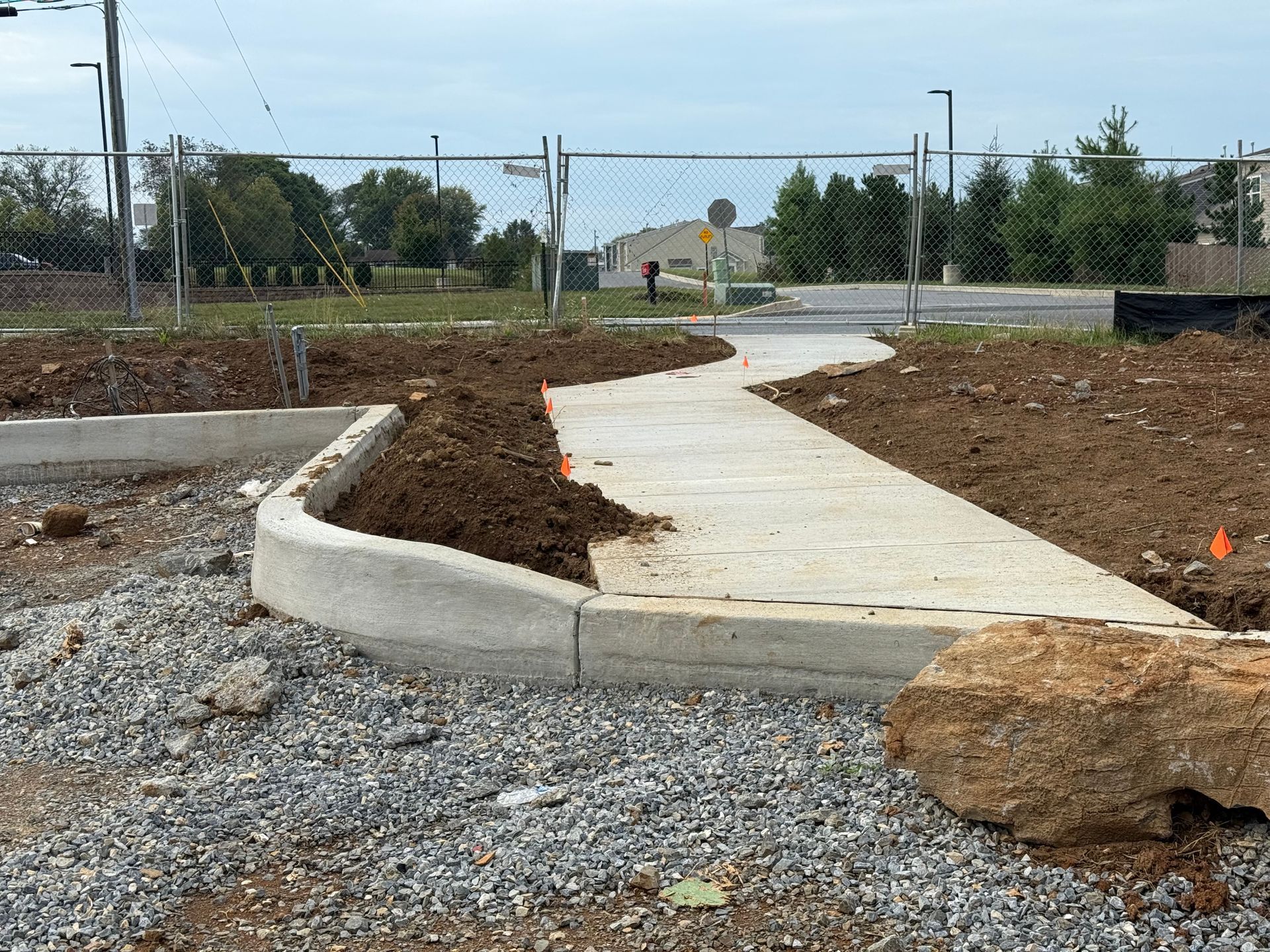 Curved concrete sidewalk under construction beside gravel and dirt in a landscaped area