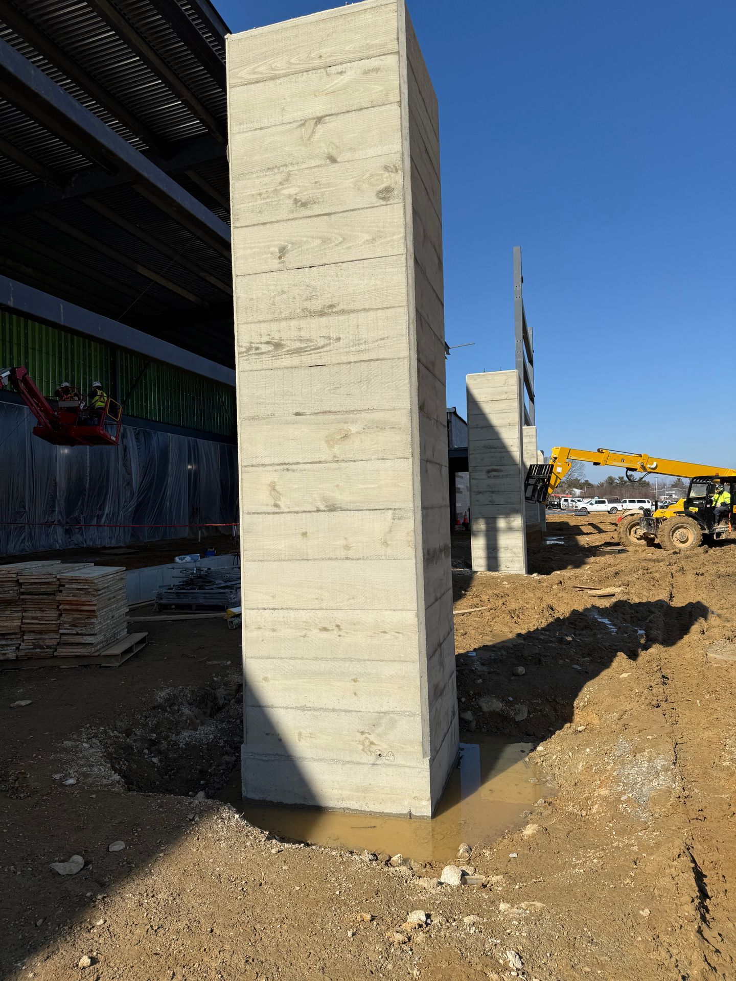 Concrete columns at a construction site beside a steel-framed building and excavator.
