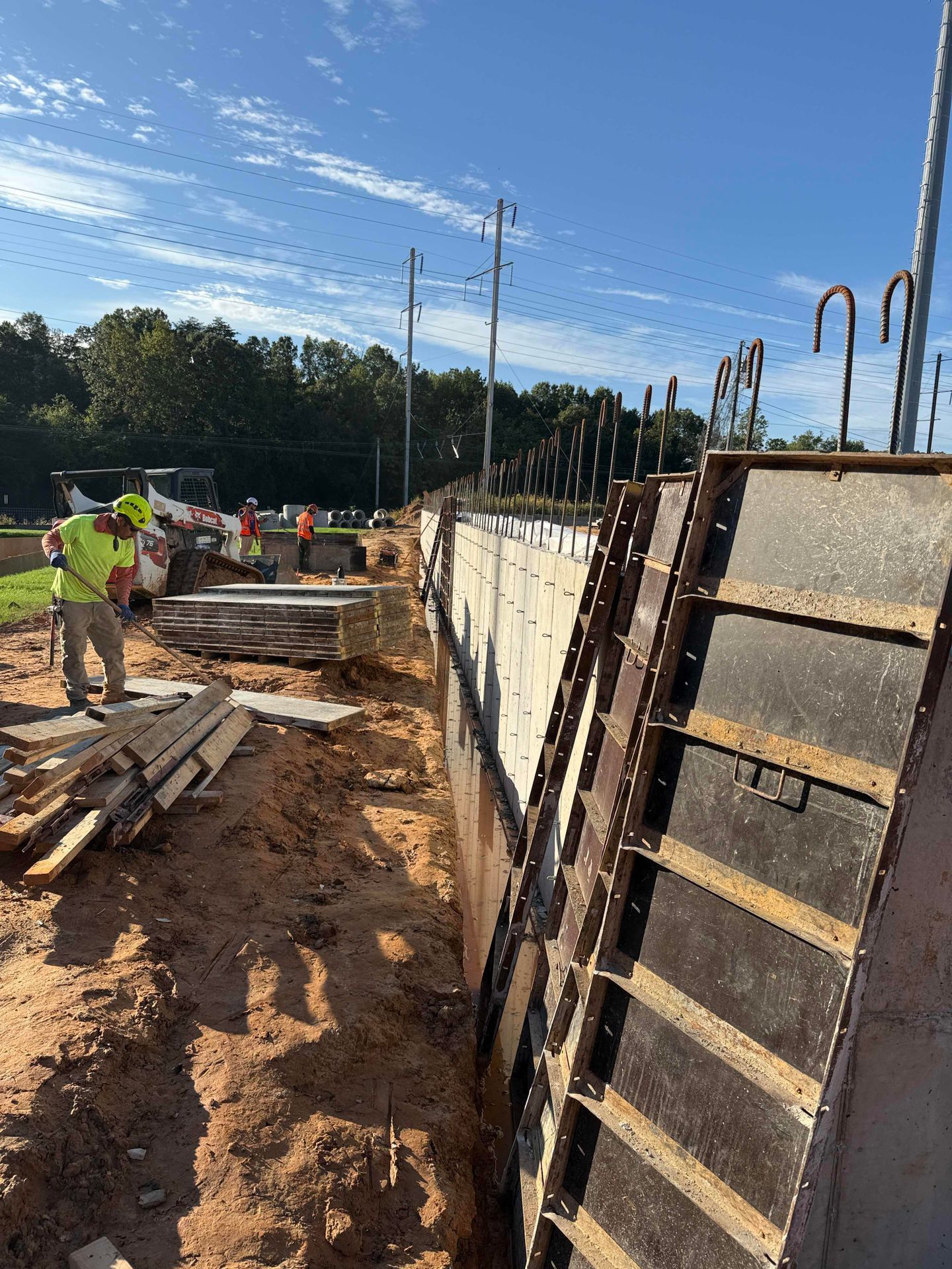 Construction workers pouring concrete along a trench beside formwork on a sunny outdoor site