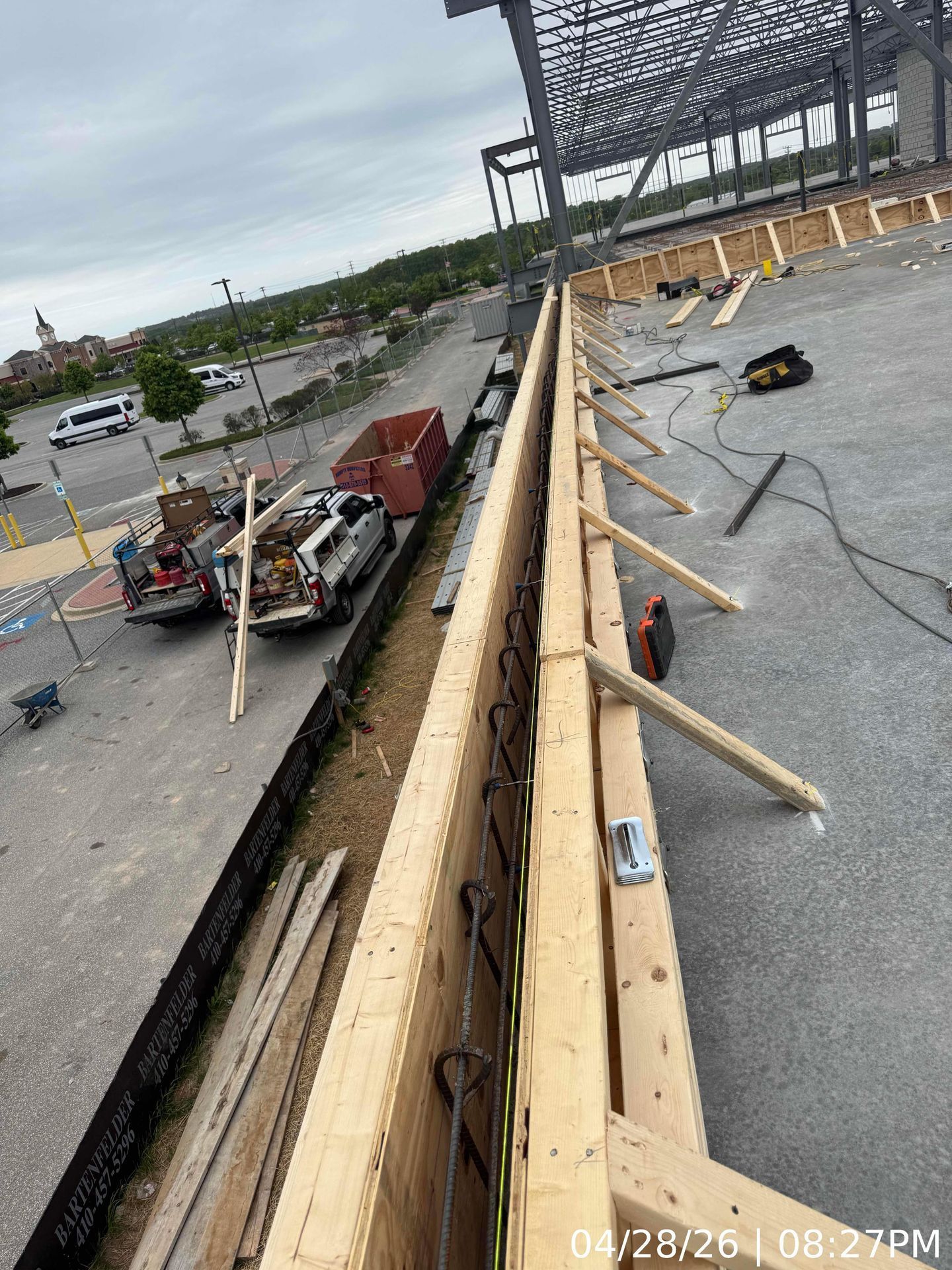 Storm damage on a rooftop with debris, roof beams, and a red pickup below in a parking lot.