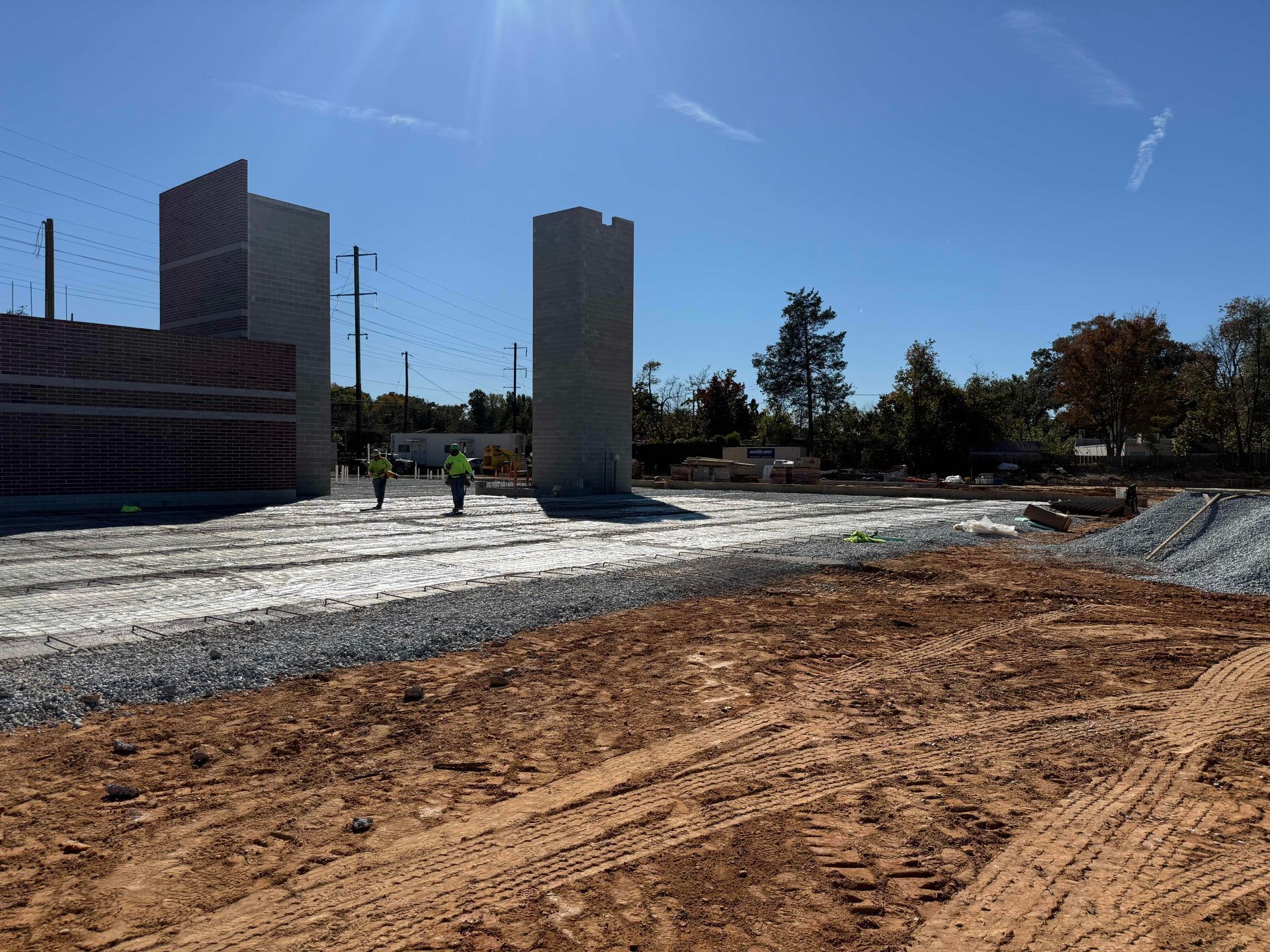 Construction site with dirt foreground, concrete pillars, and a partially built brick structure under a blue sky