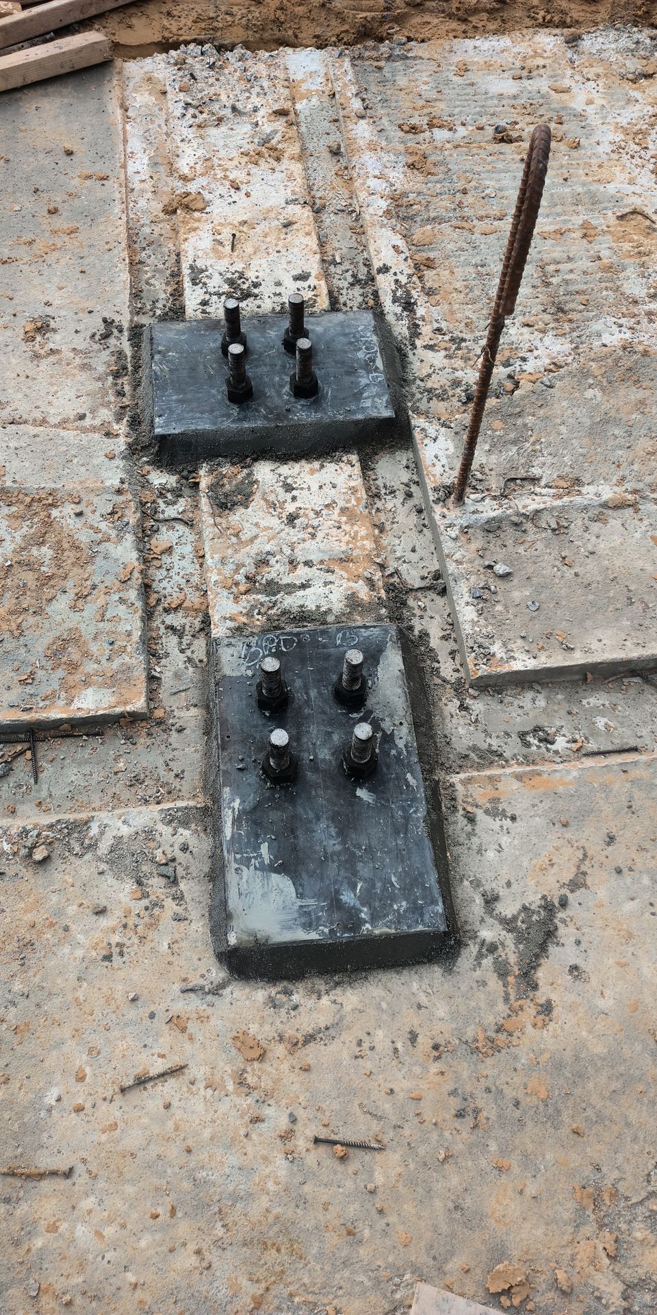 Two black metal plates with bolts on a tiled stone floor beside a rusted rod