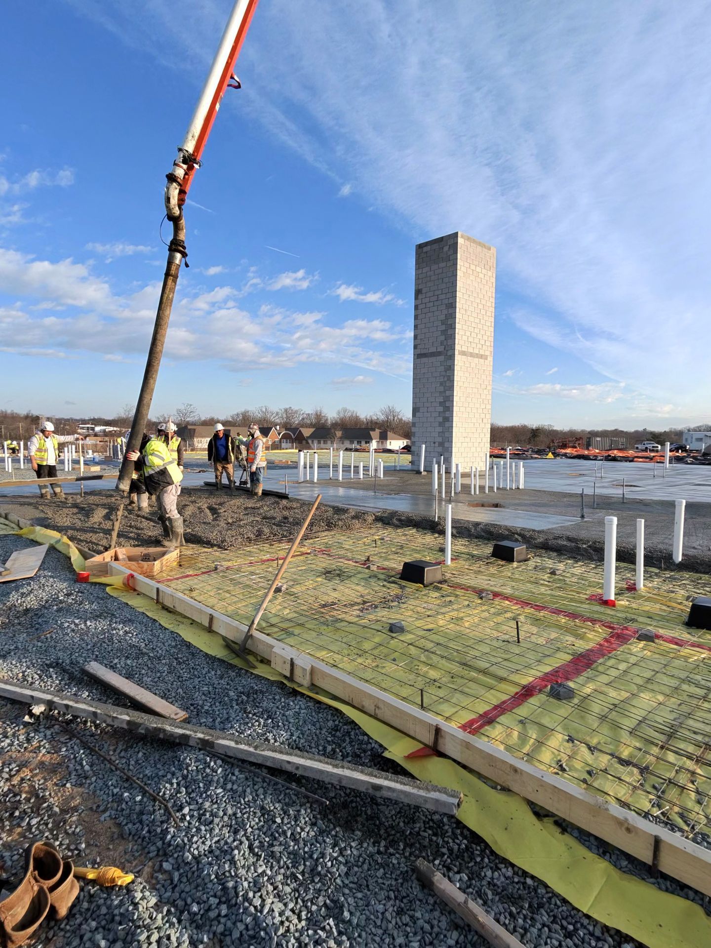 Construction site with concrete slab being poured by crane beside a tall rectangular tower