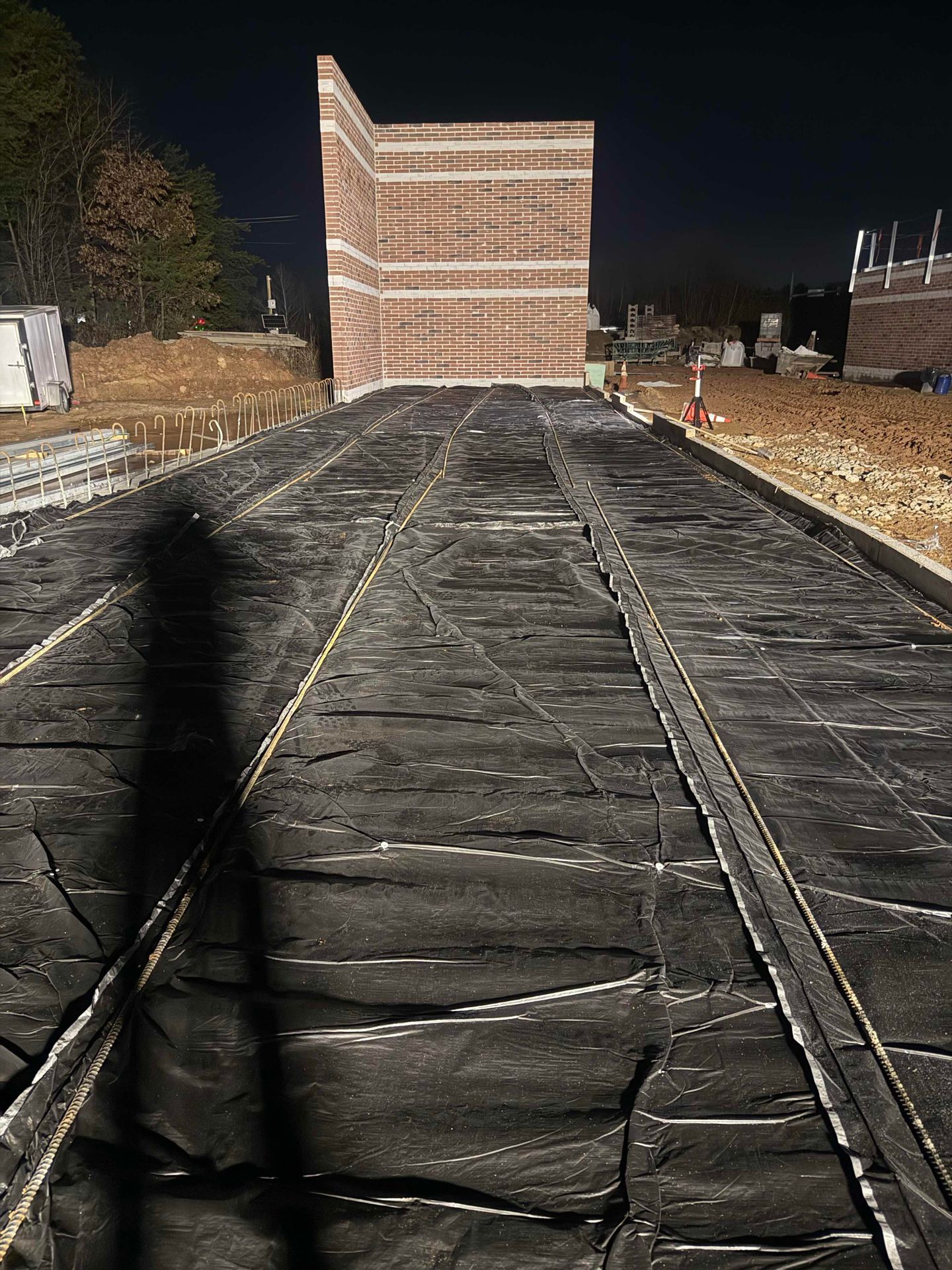 Covered path leads to a lit brick building at night, with construction materials and bare ground on both sides.