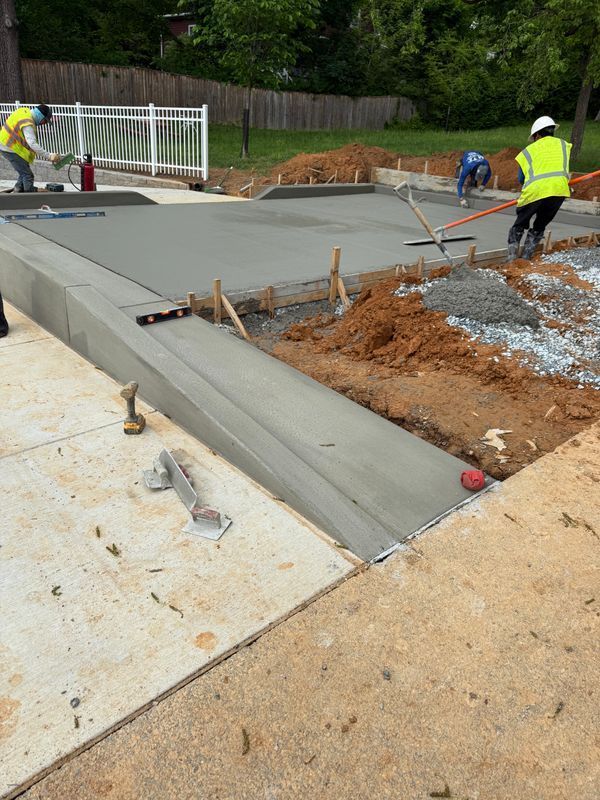 Workers pouring concrete for a new sidewalk ramp at a construction site