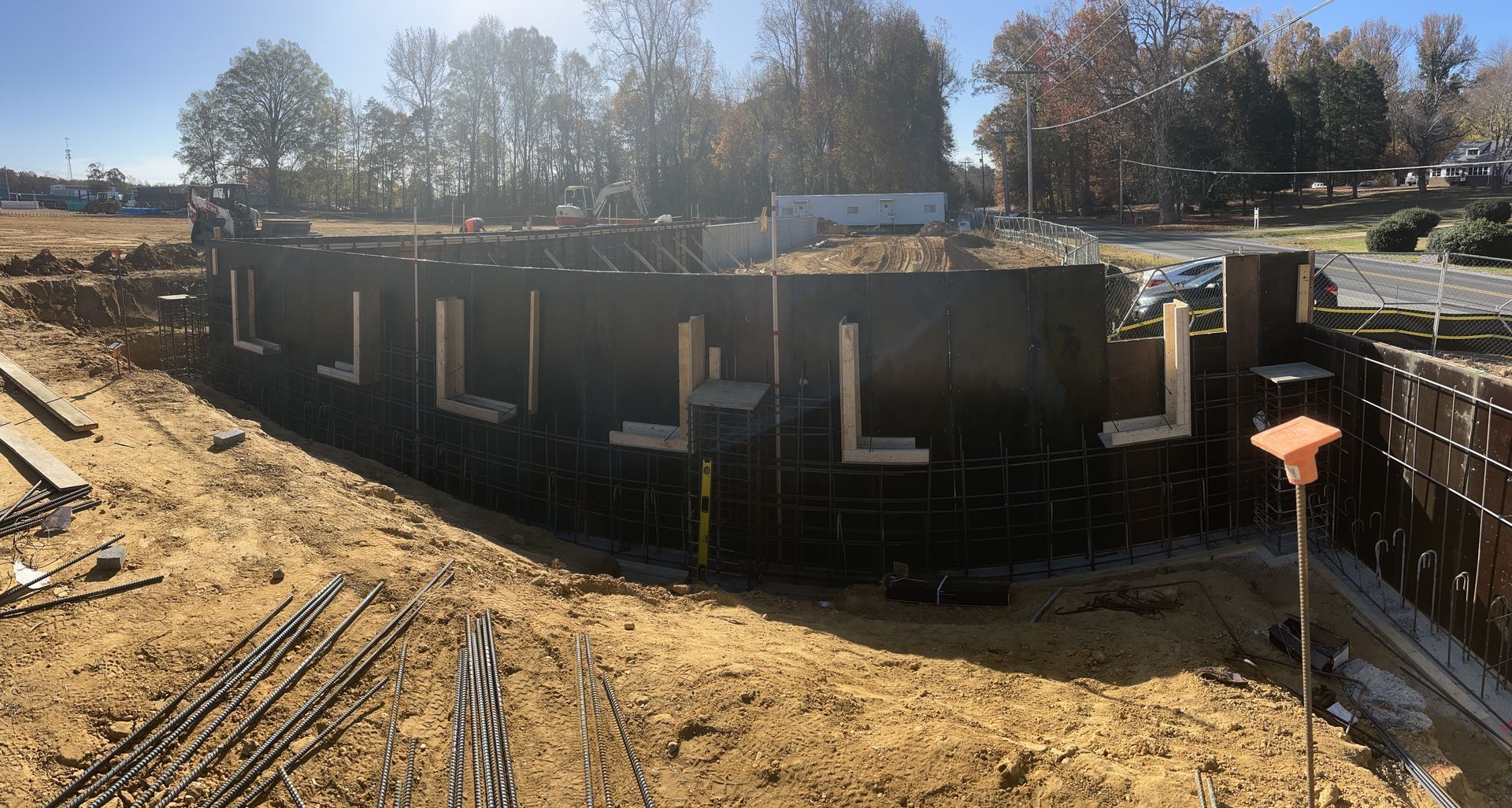 Round black concrete structure under construction on a dirt lot, with scaffolding and trees in the background