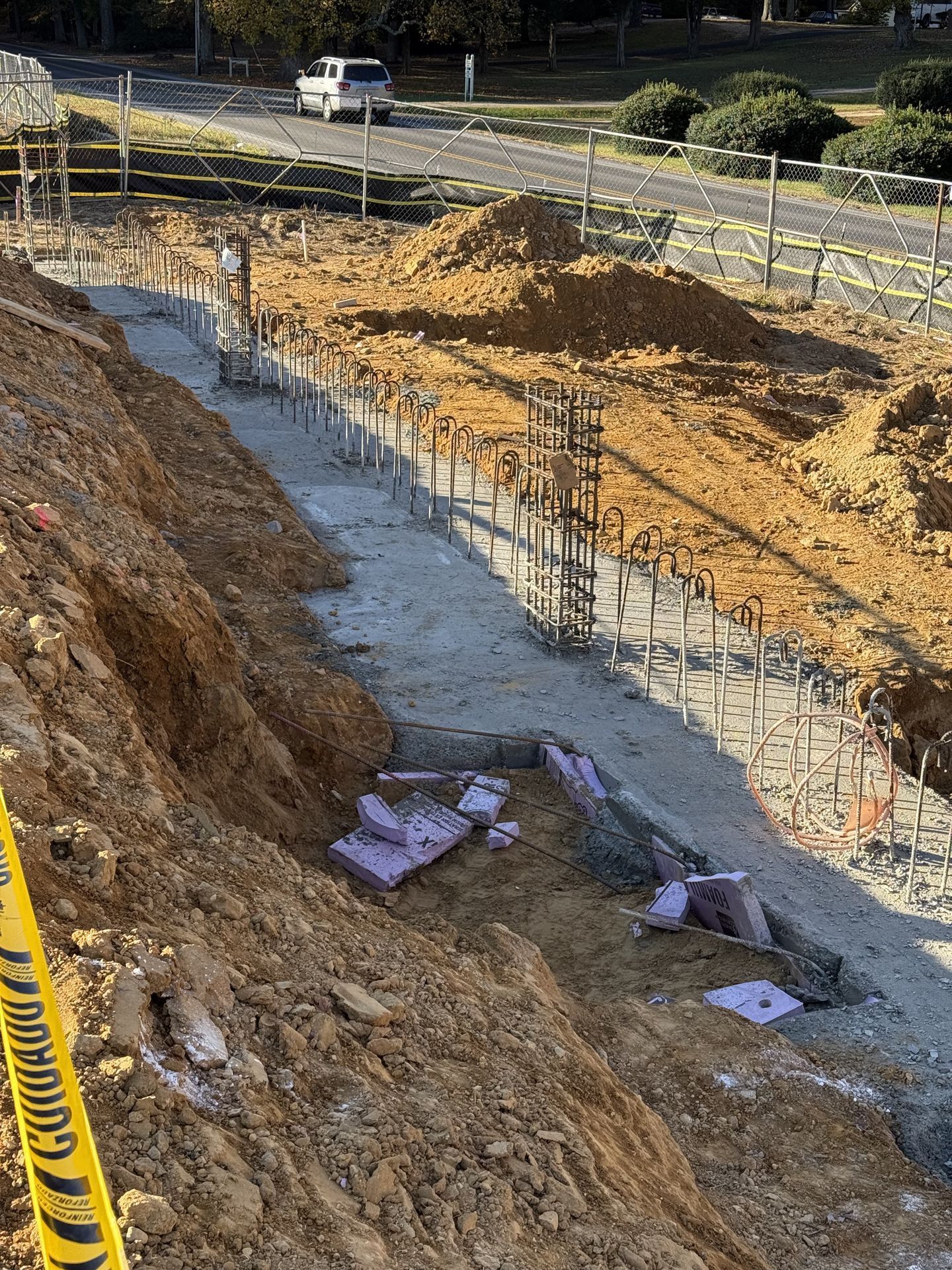 Construction trench with rebar and concrete, bordered by dirt embankments and caution tape.