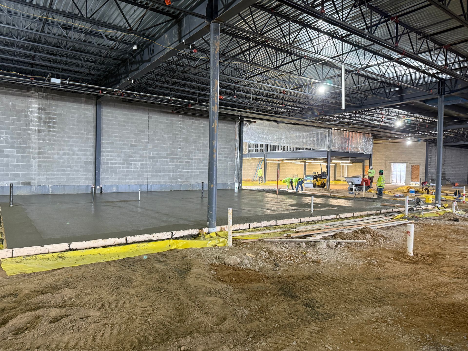 Large unfinished warehouse interior with concrete floor, exposed ceiling beams, and construction materials.