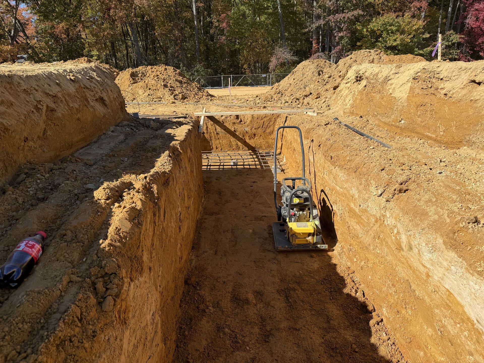 Yellow excavator in a deep dirt trench at a construction site with an RC car on the left ledge