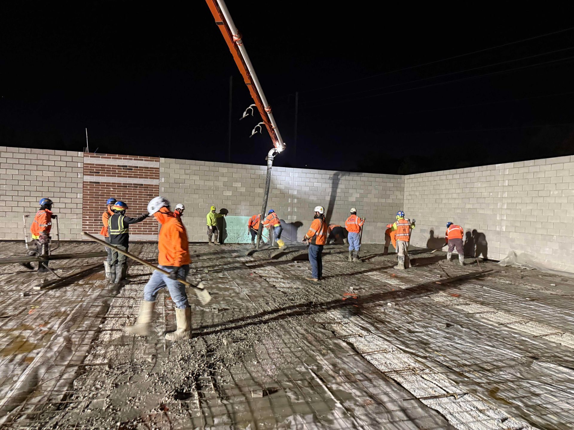 Construction workers in orange vests smoothing concrete on a large nighttime foundation pour