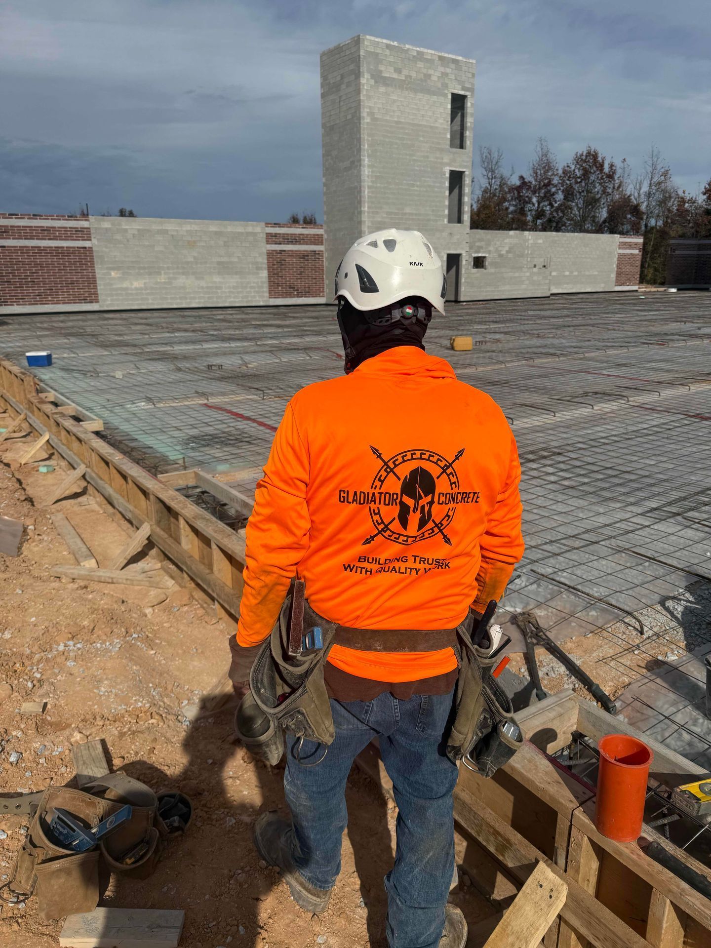 Worker in orange jacket and white hard hat standing on a rooftop construction site.