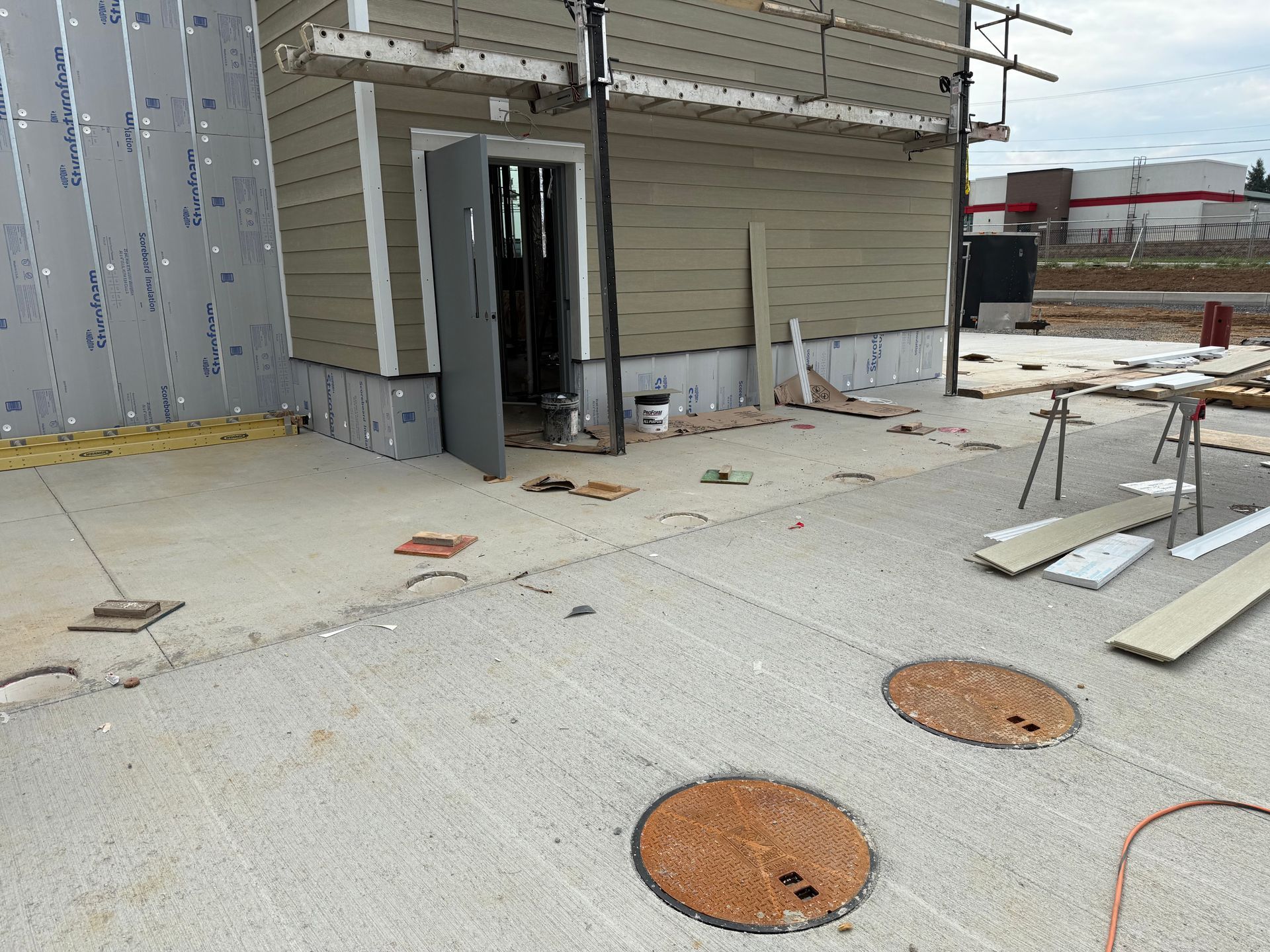 Construction site with unfinished building exterior, concrete ground, and scattered materials near an open doorway