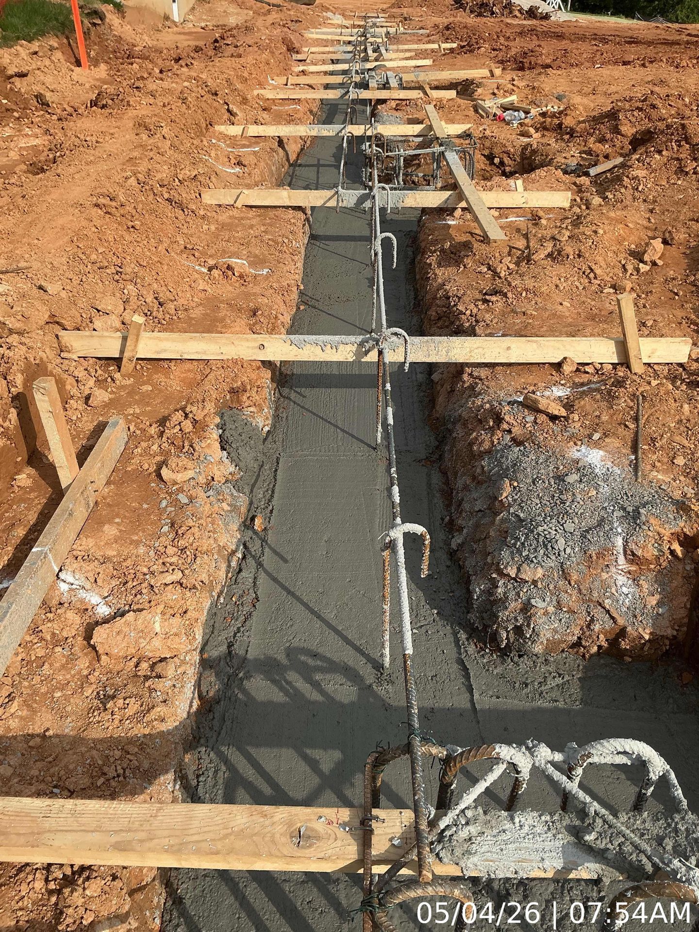 Concrete foundation trench with rebar and wooden braces at a construction site