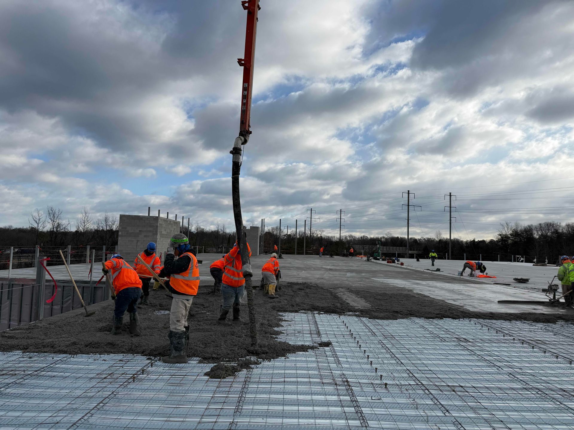 Construction workers in orange vests pouring concrete on a large slab under cloudy skies