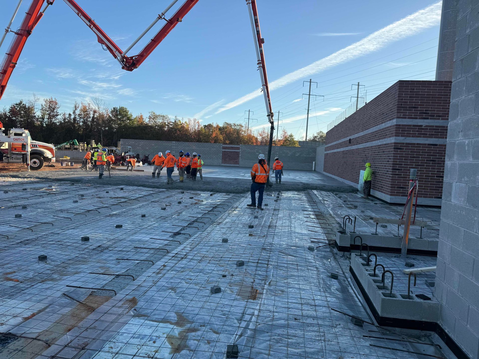 Construction workers in orange vests on a large concrete site with crane arms overhead.