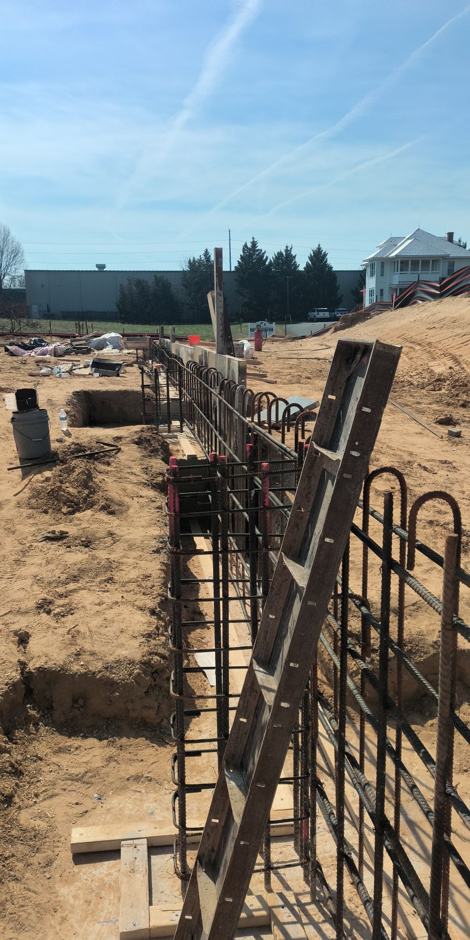 Construction site with rebar foundation trenches and wooden forms under a clear blue sky