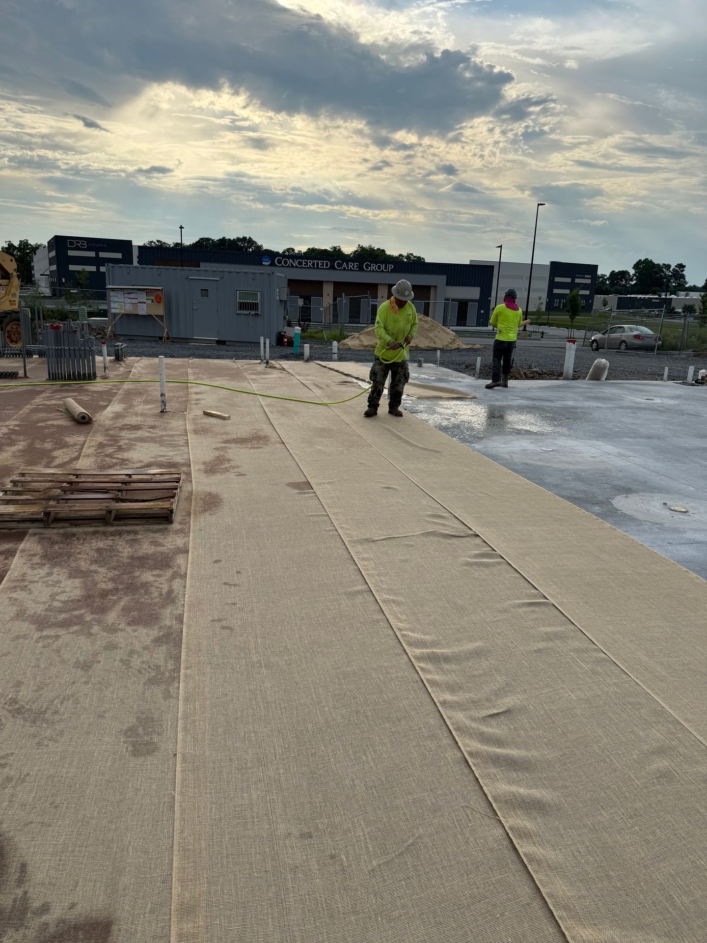 Construction site with two workers in yellow vests on a large concrete slab at sunrise.