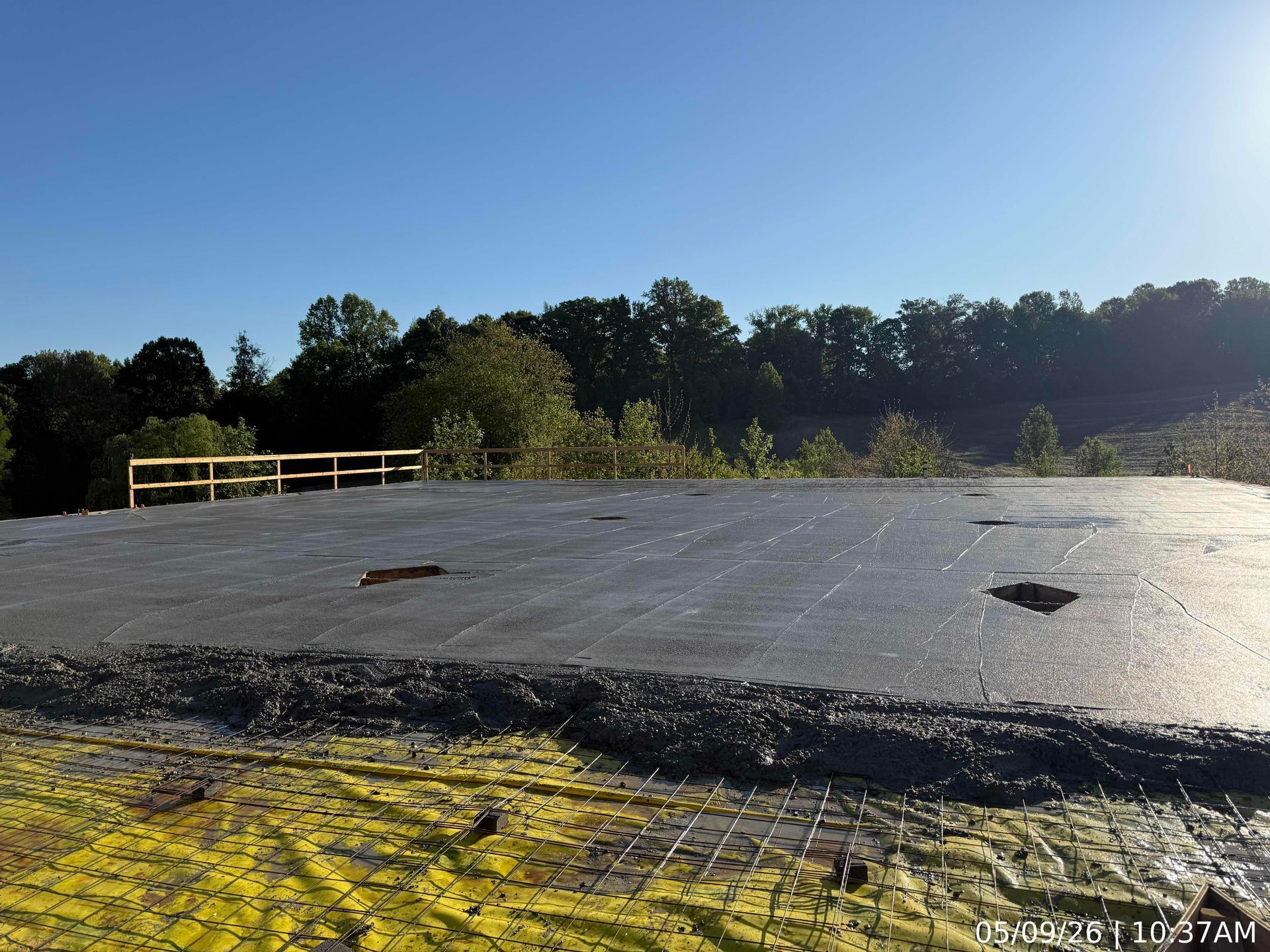 Concrete platform with yellow railing under a blue sky beside a wooded area
