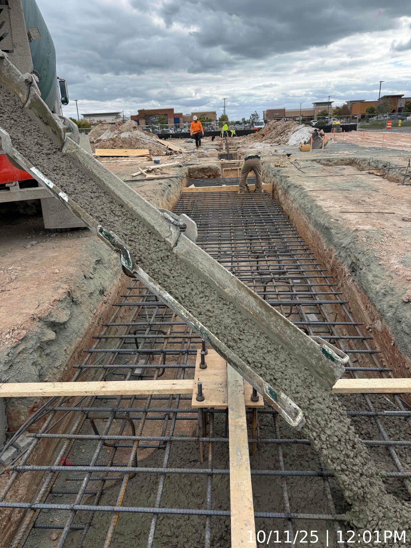 Concrete bridge construction with rebar and formwork on a roadway, workers in the distance.