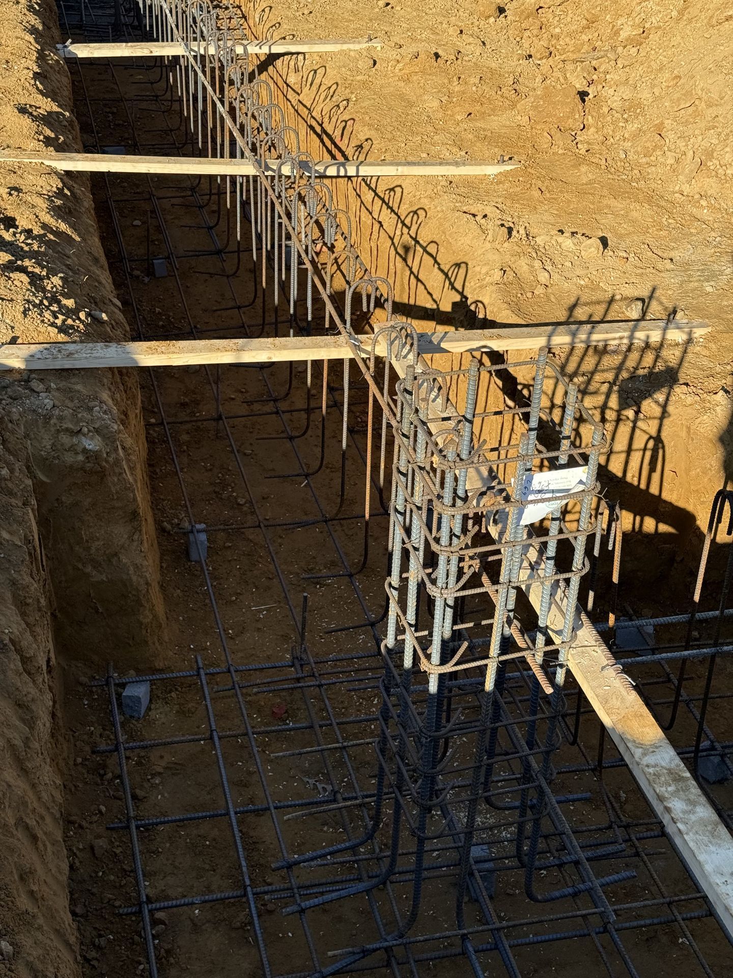 Rebar cage and wooden formwork in a deep construction excavation under sandy soil.