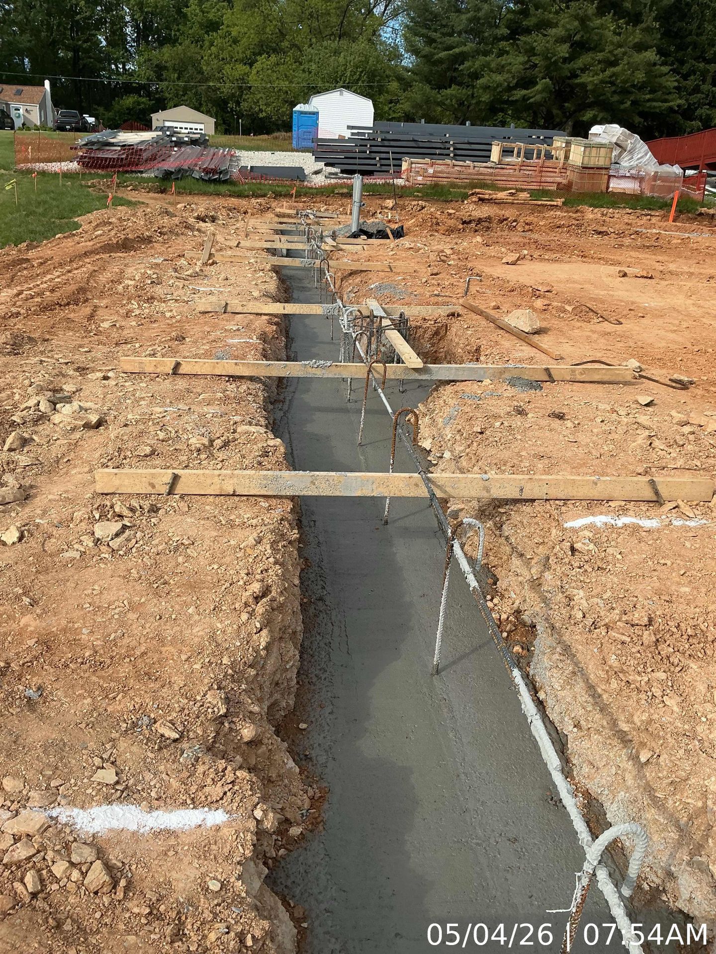 Fresh concrete trench at a construction site, with wooden planks spanning the excavation.