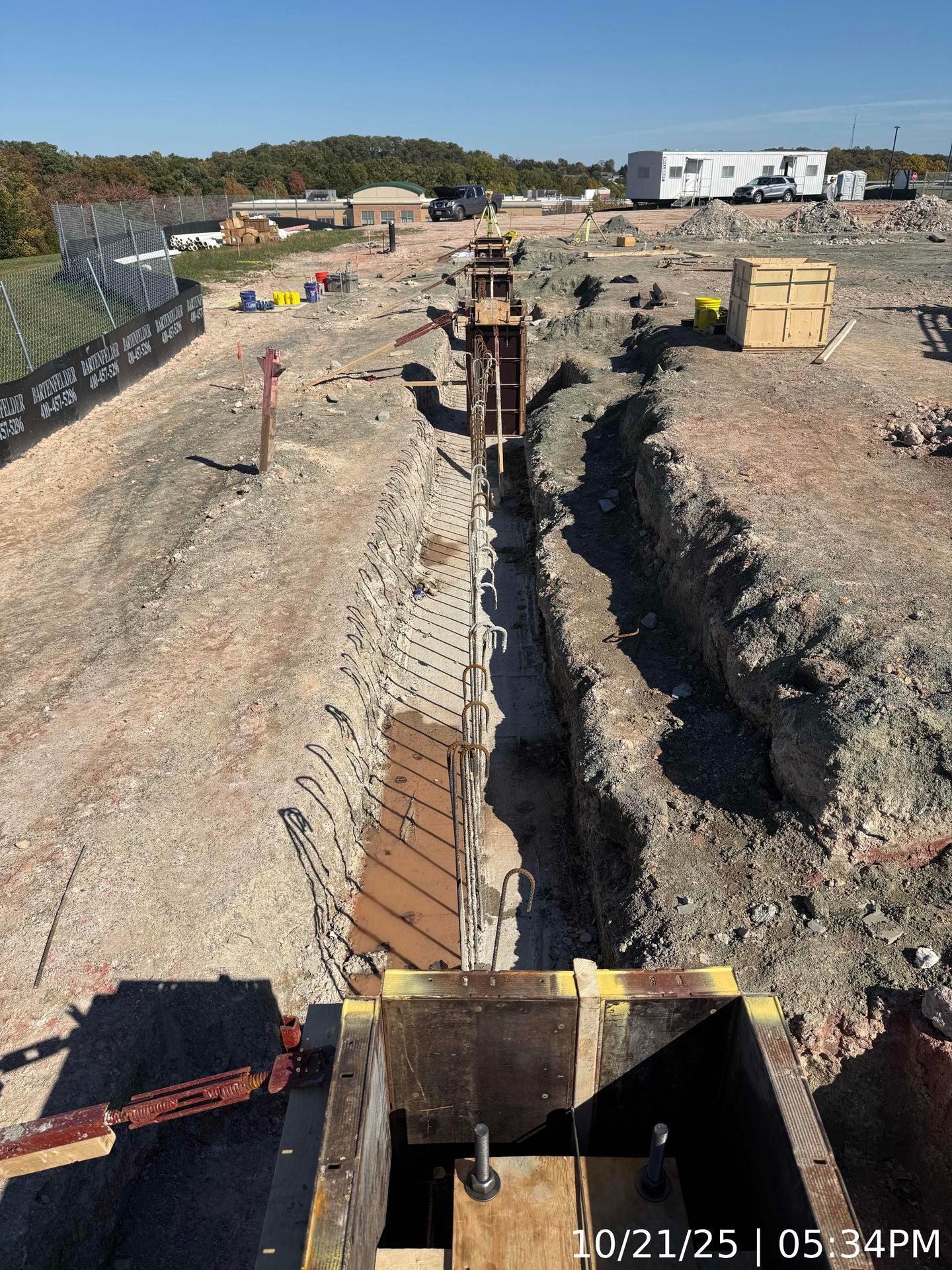 Construction trench with exposed rebar and wooden formwork in a dirt site under clear daylight.
