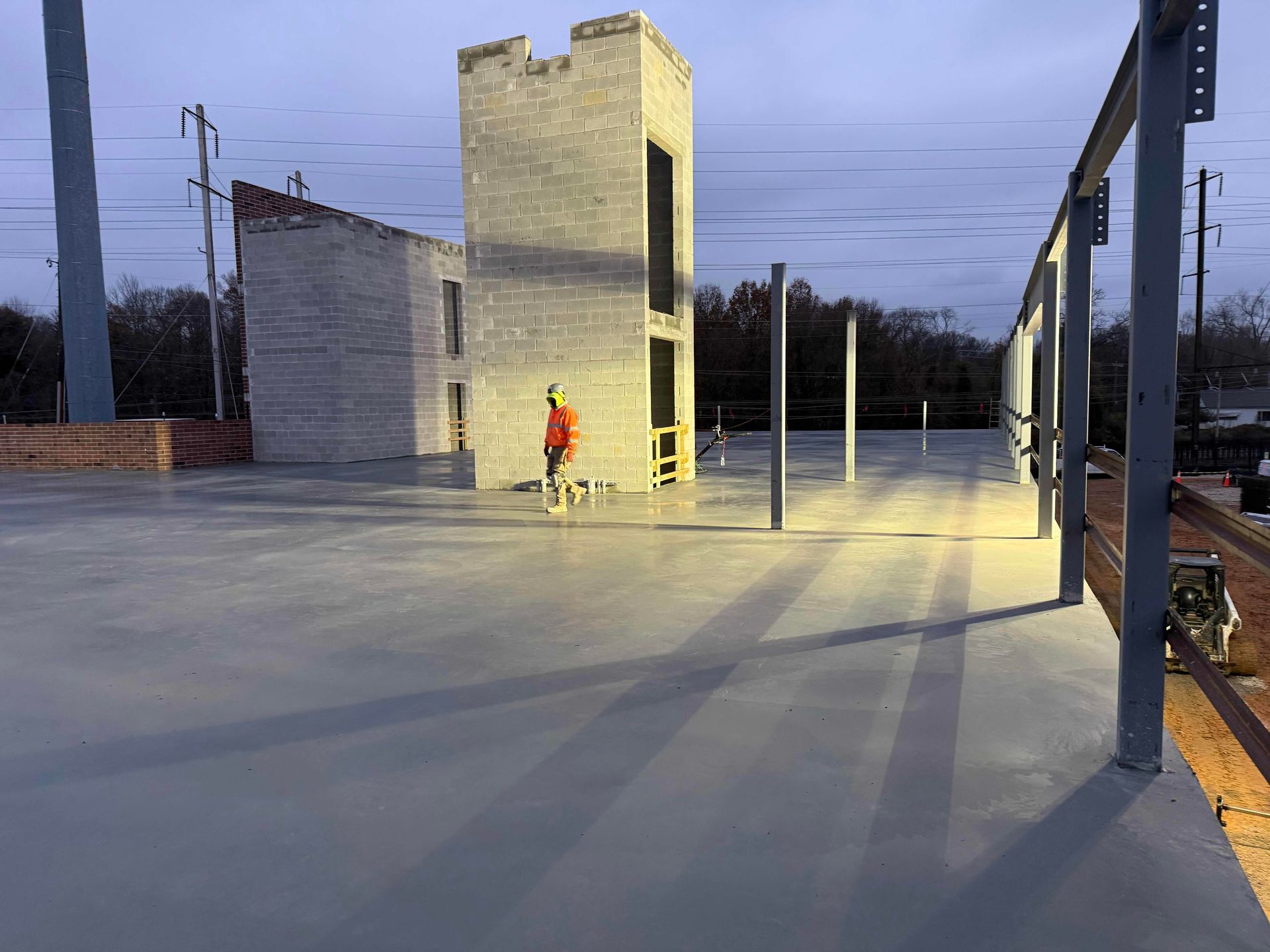 Empty concrete lot with a small unfinished building and one person in a red jacket at dusk
