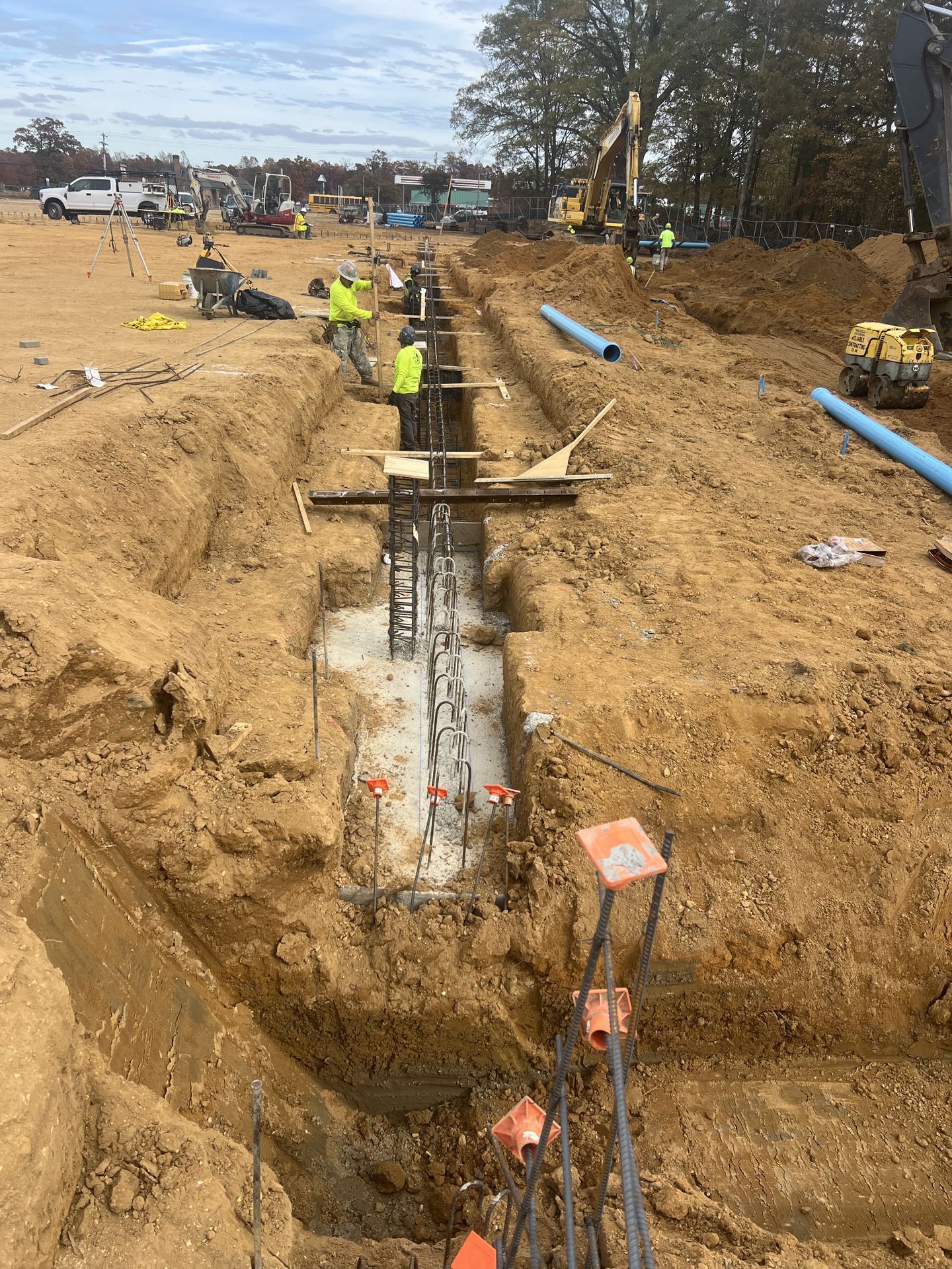 Utility workers digging a trench around a concrete foundation at an active construction site