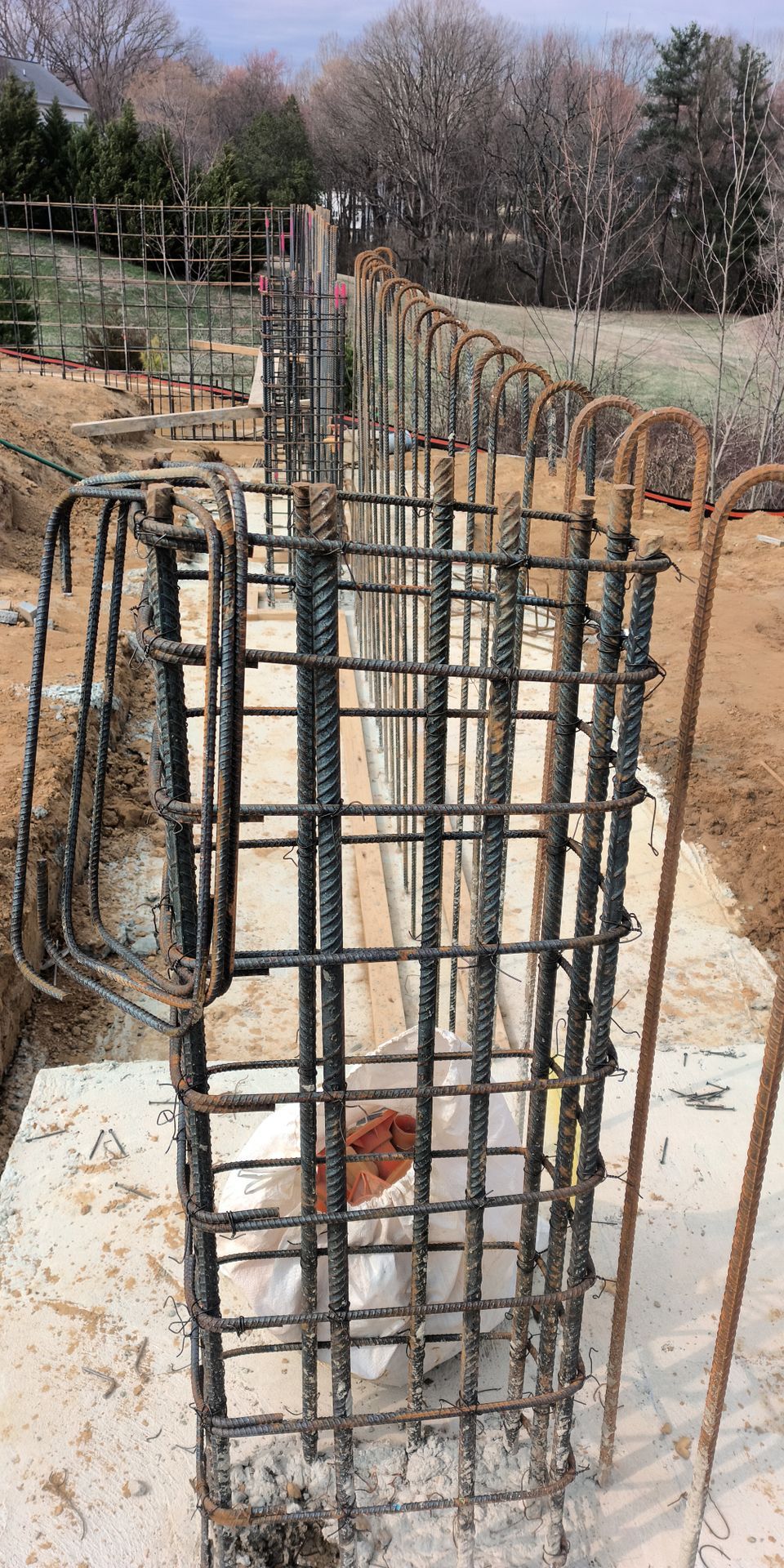 Steel rebar column cage rising from a concrete slab at a construction site, with trees in the background
