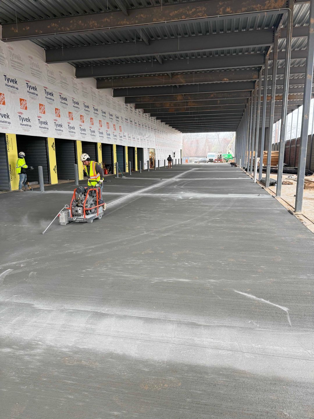 Workers smoothing a large concrete floor inside a warehouse with exposed steel beams
